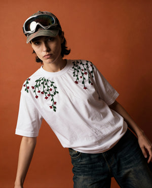 Person wearing a white t-shirt with floral embroidery against an orange background