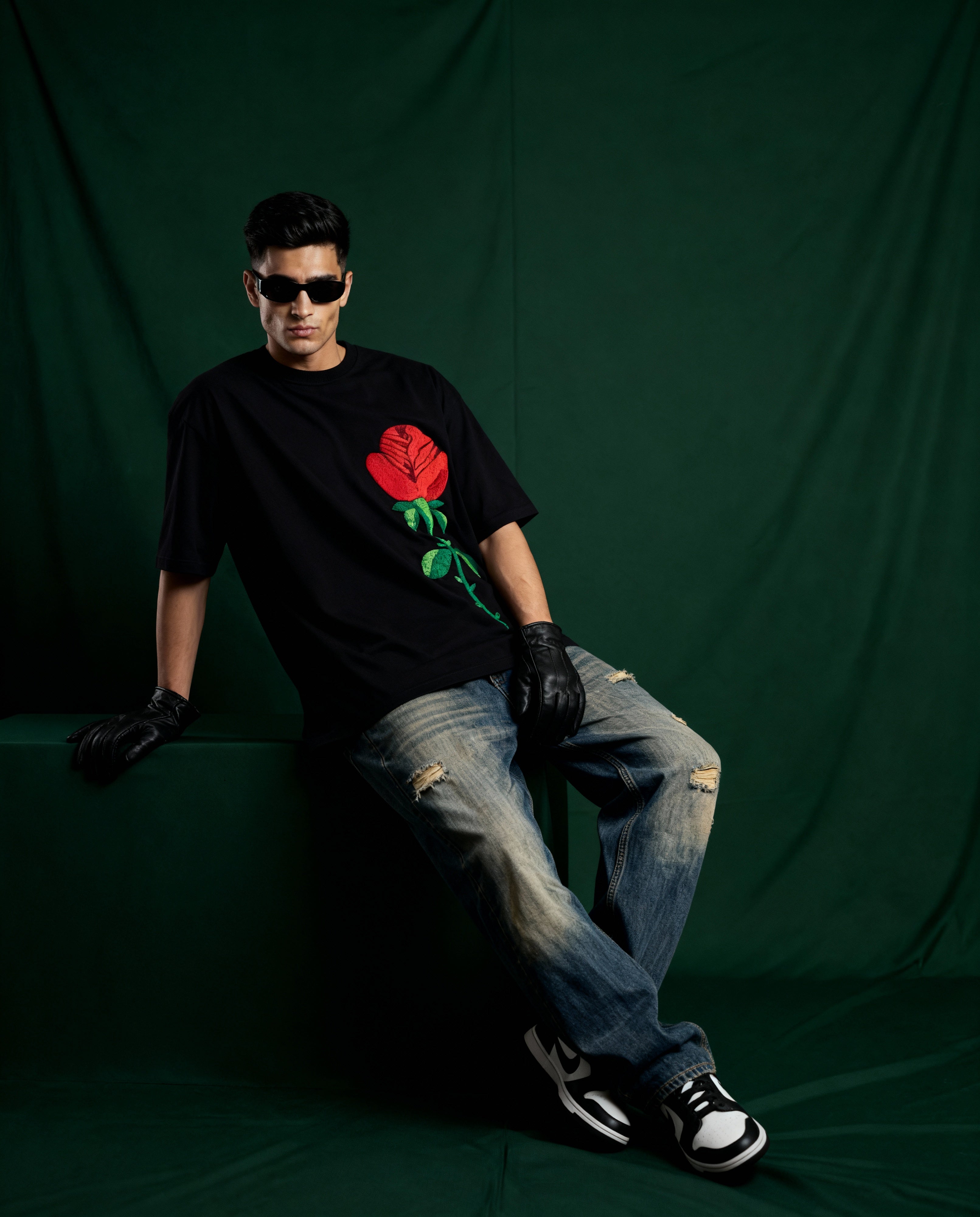 Person wearing a black t-shirt with a red rose design, sitting against a green backdrop.