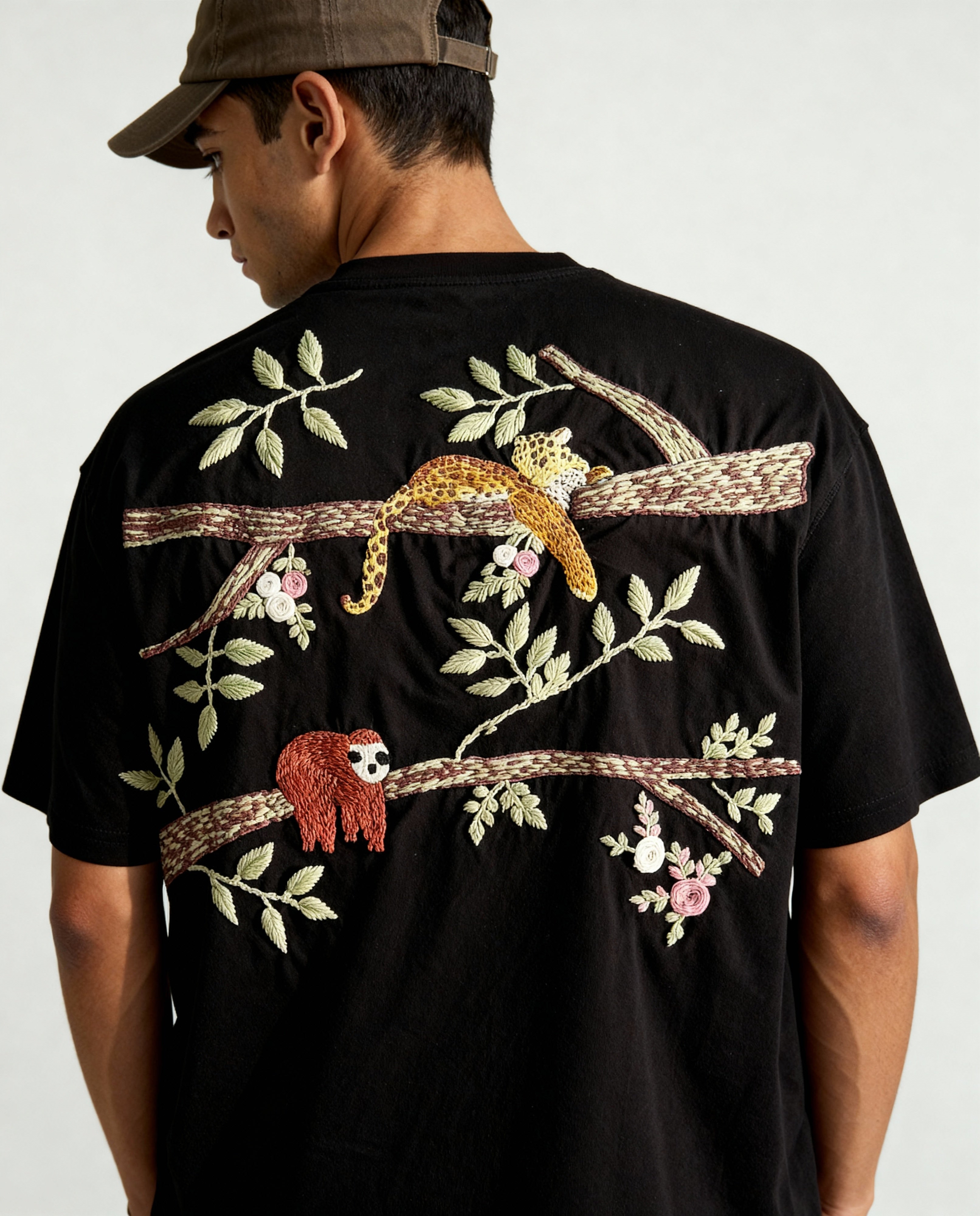 Person wearing a black t-shirt with colorful embroidered designs of sloths and foliage on a plain background
