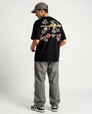 Person wearing a black t-shirt with floral designs hand embroidered on the back, standing against a white background