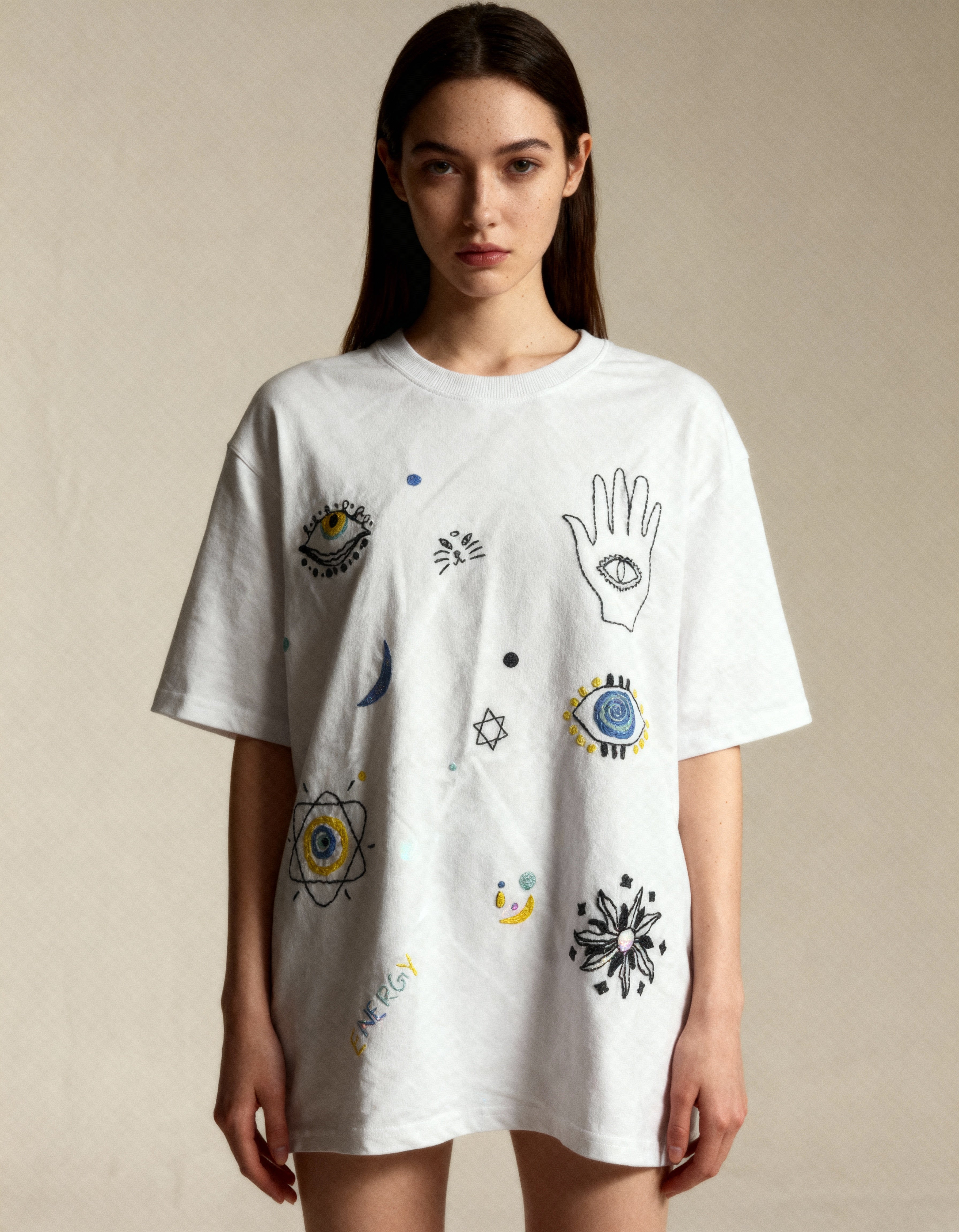 Model wearing a white t-shirt with various symbols and designs on a beige background