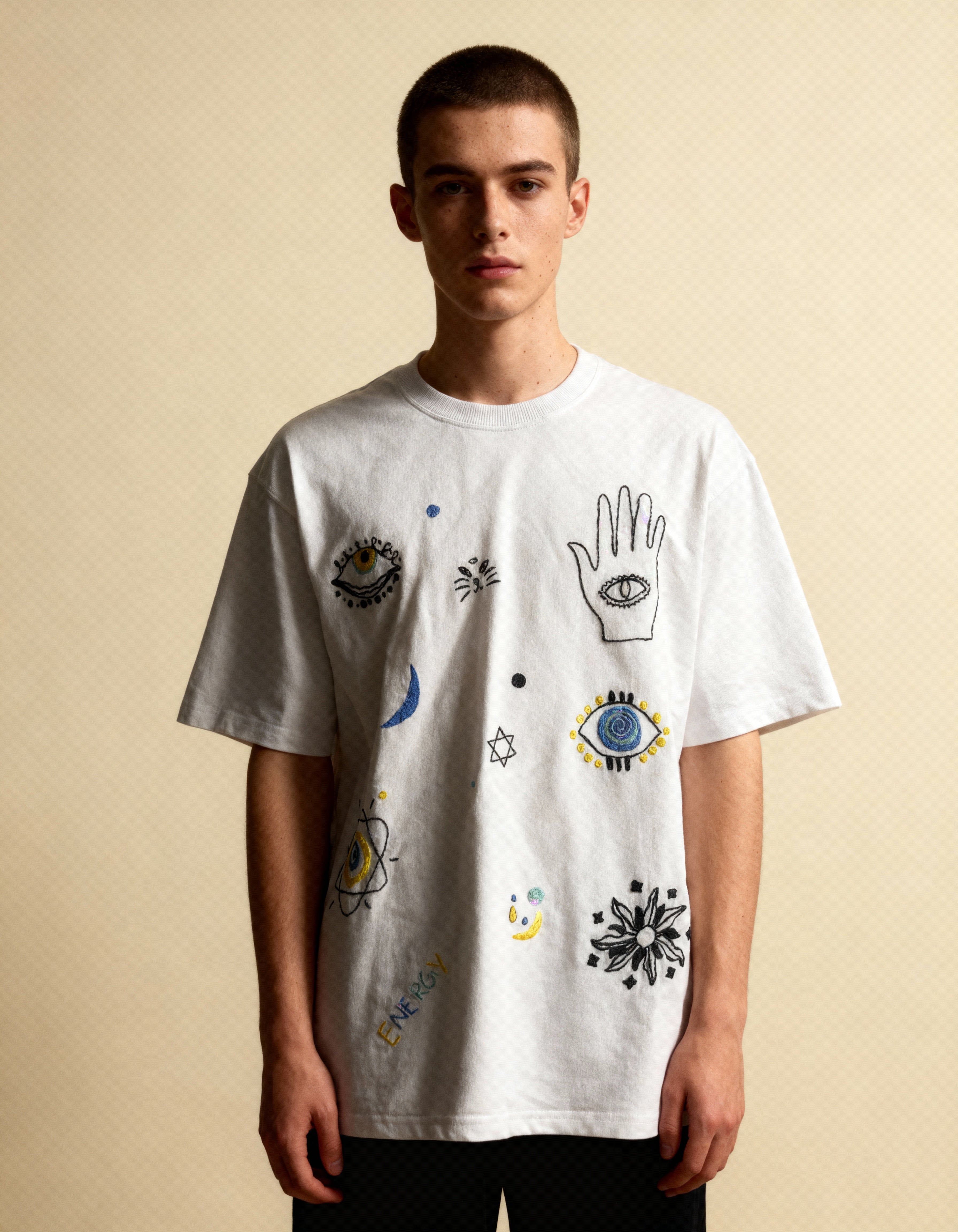Hand embroidered cotton tee symbols — person wearing white cotton tee with hand-embroidered various cosmic symbols on beige background
