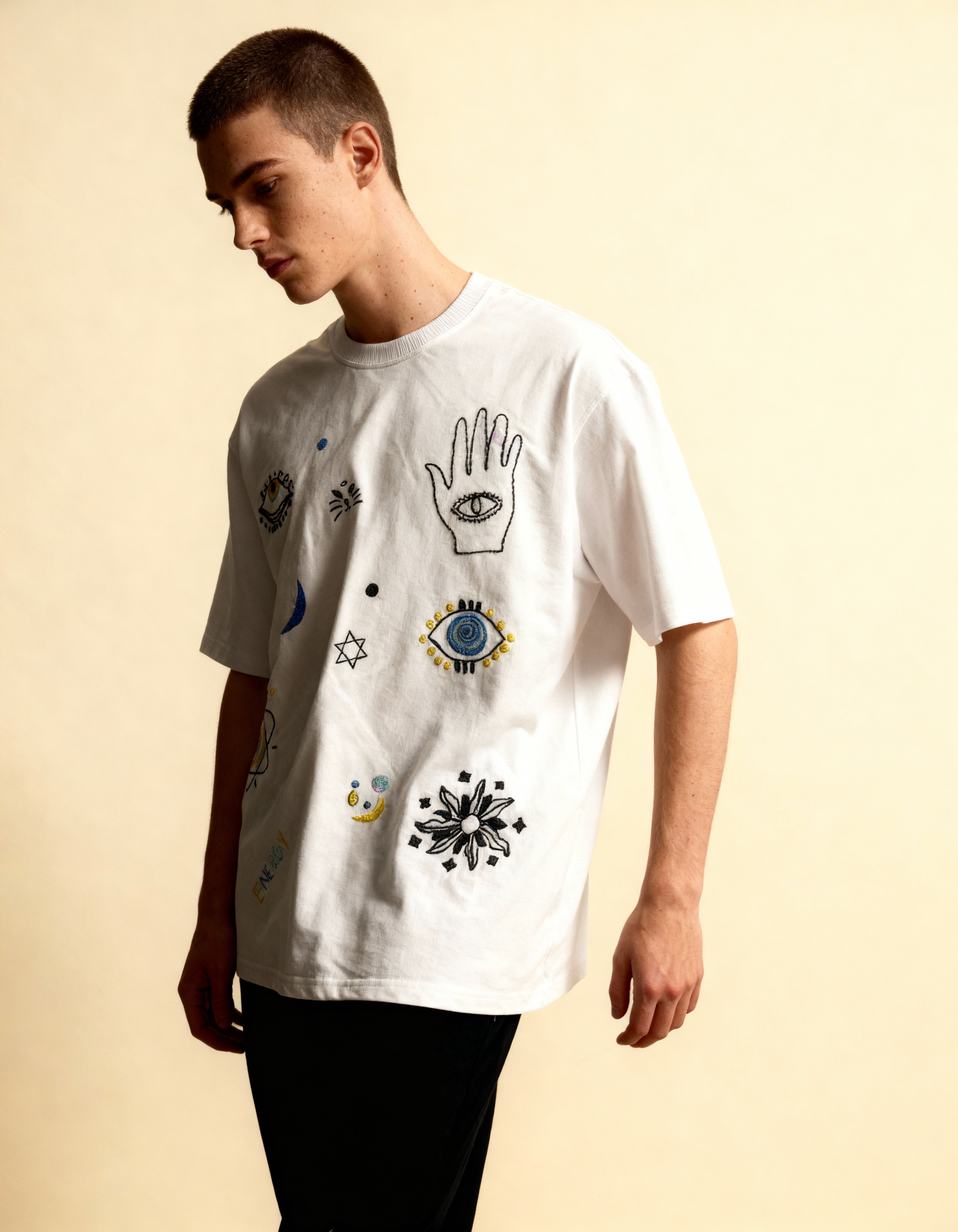 Person wearing a white t-shirt with embroidered various symbols on a beige background