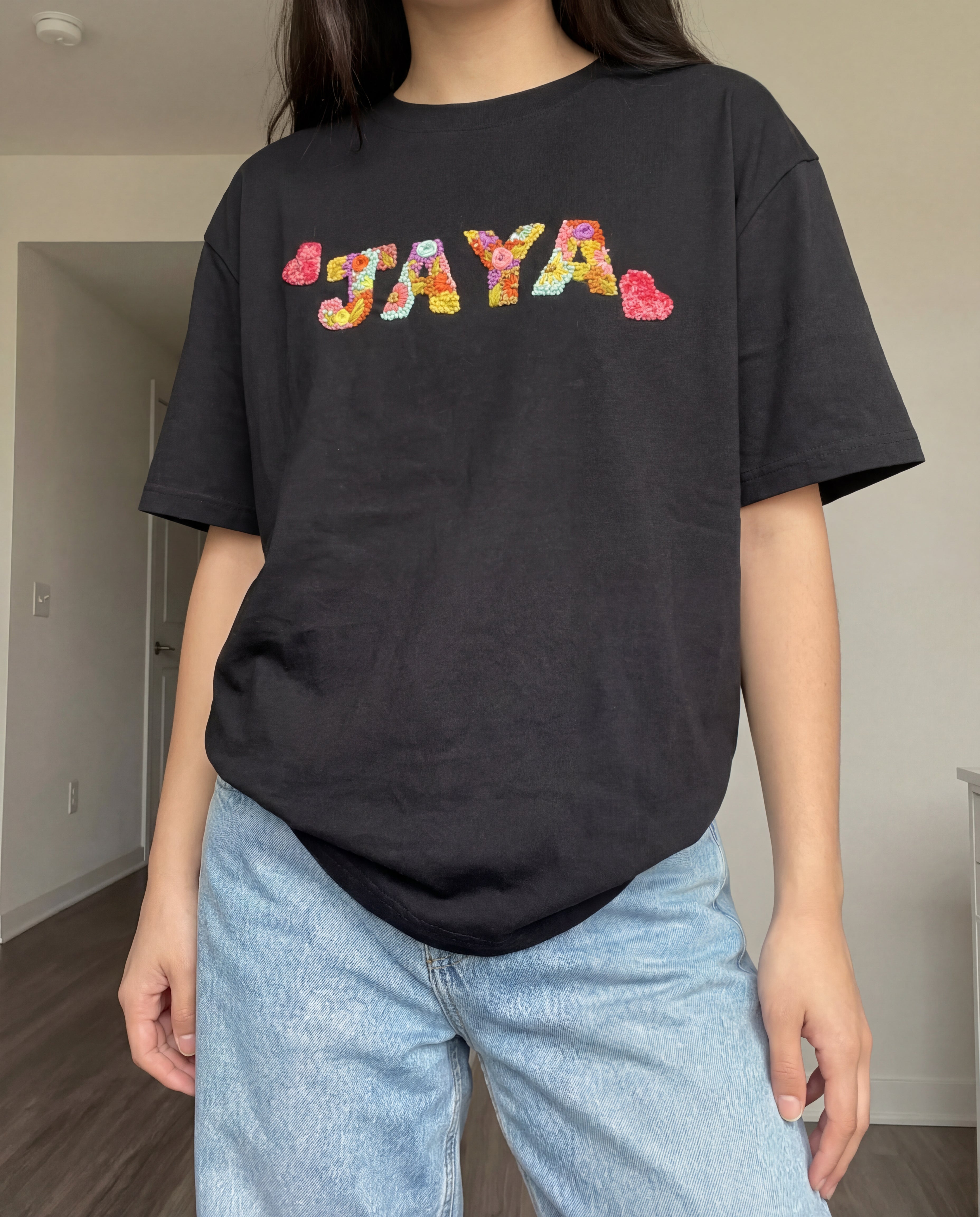 Person wearing a black t-shirt with 'JAYA' in colorful letters hand embroidered