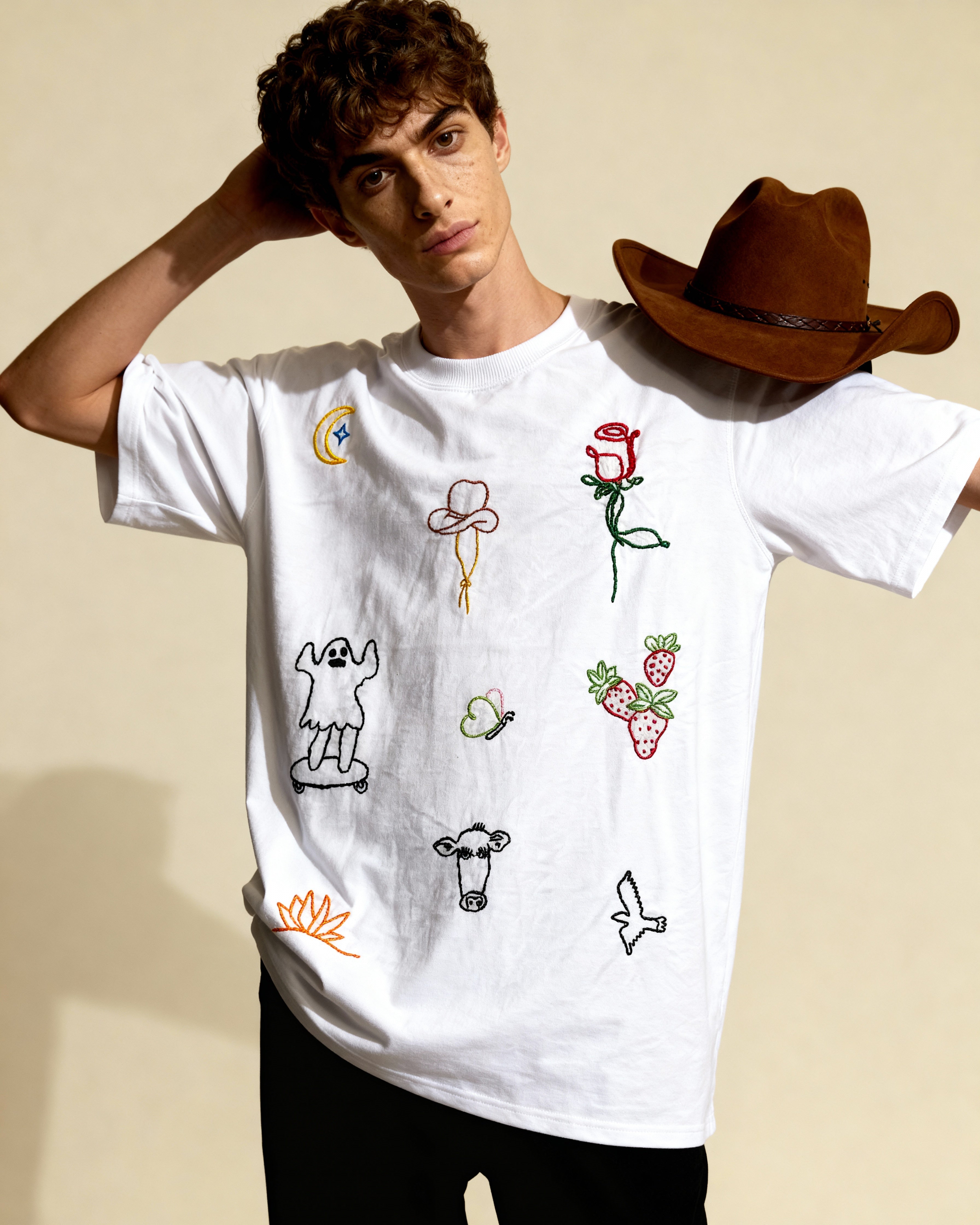 Person wearing a white t-shirt with various embroidered designs on a beige background