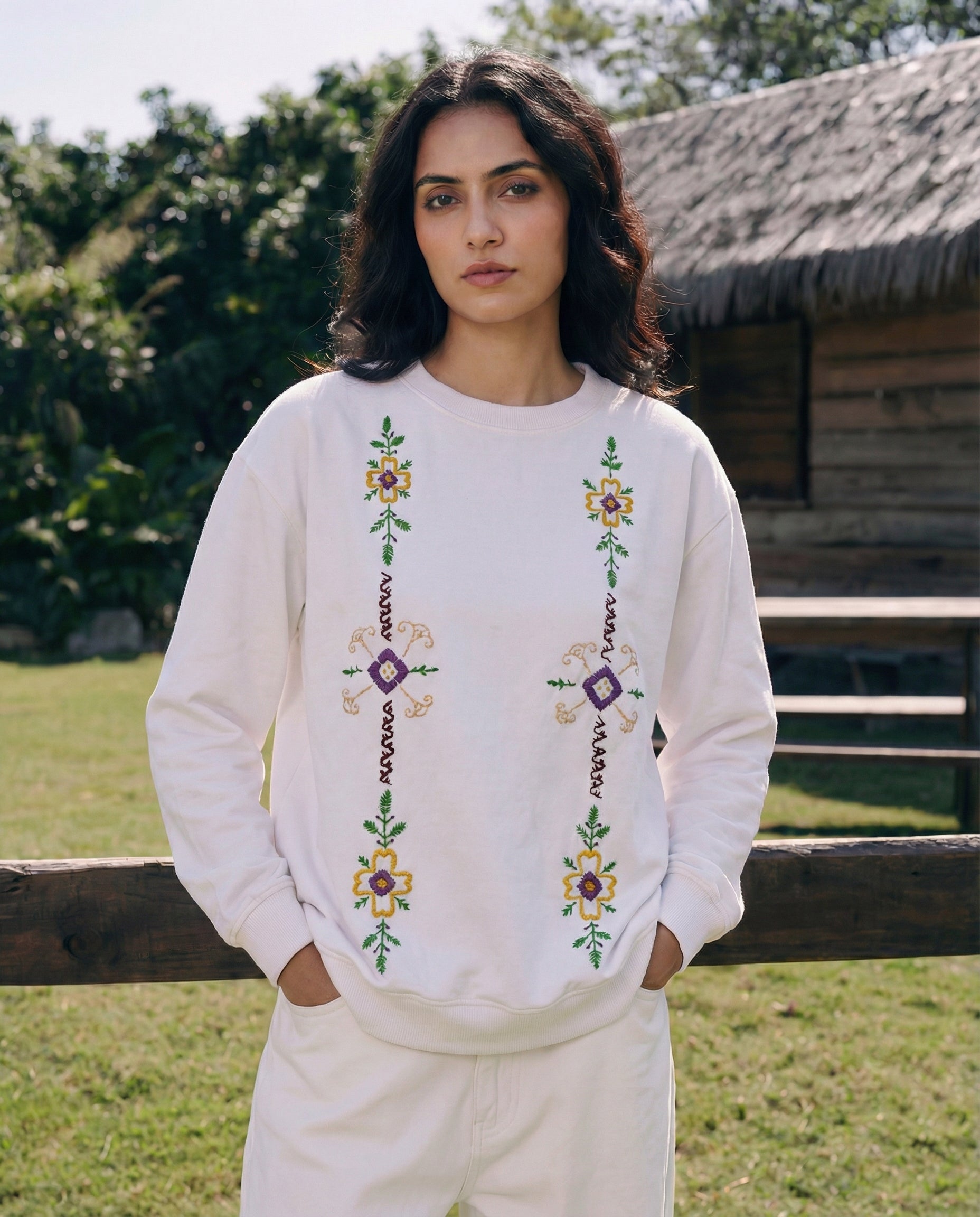Woman wearing a white embroidered sweater and pants outdoors.