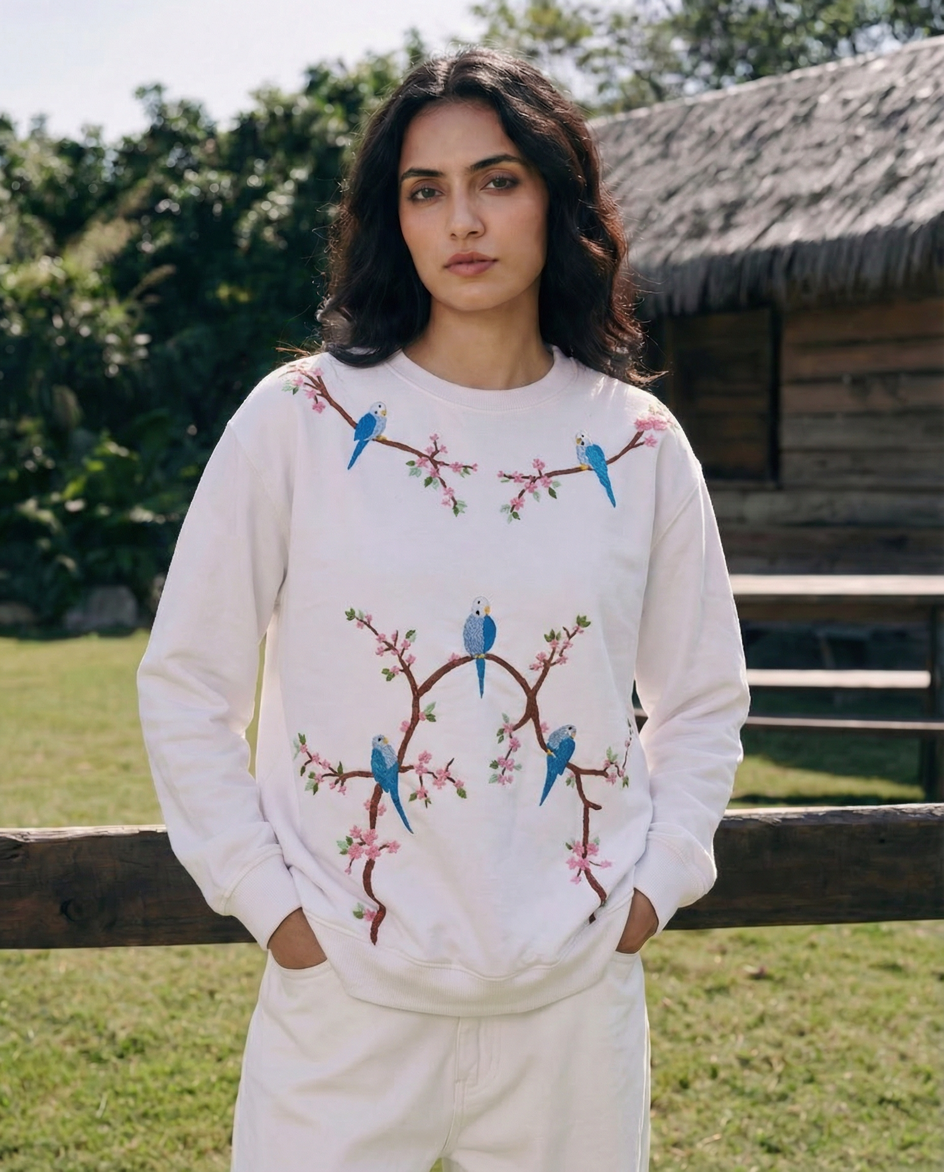 Woman wearing a white embroidered sweatshirt with bird designs outdoors