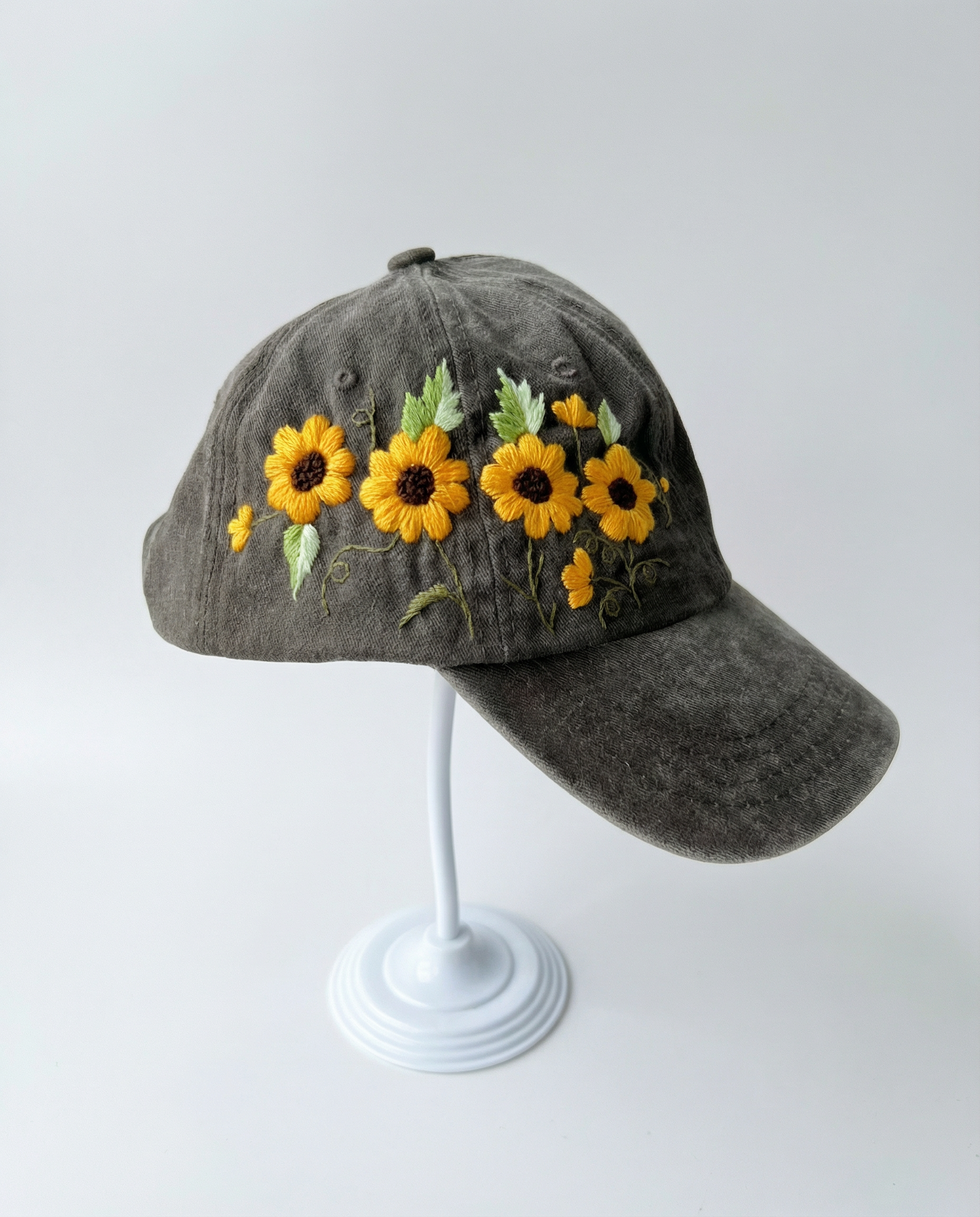 Gray cap with sunflower embroidery on a white stand against a light gray background