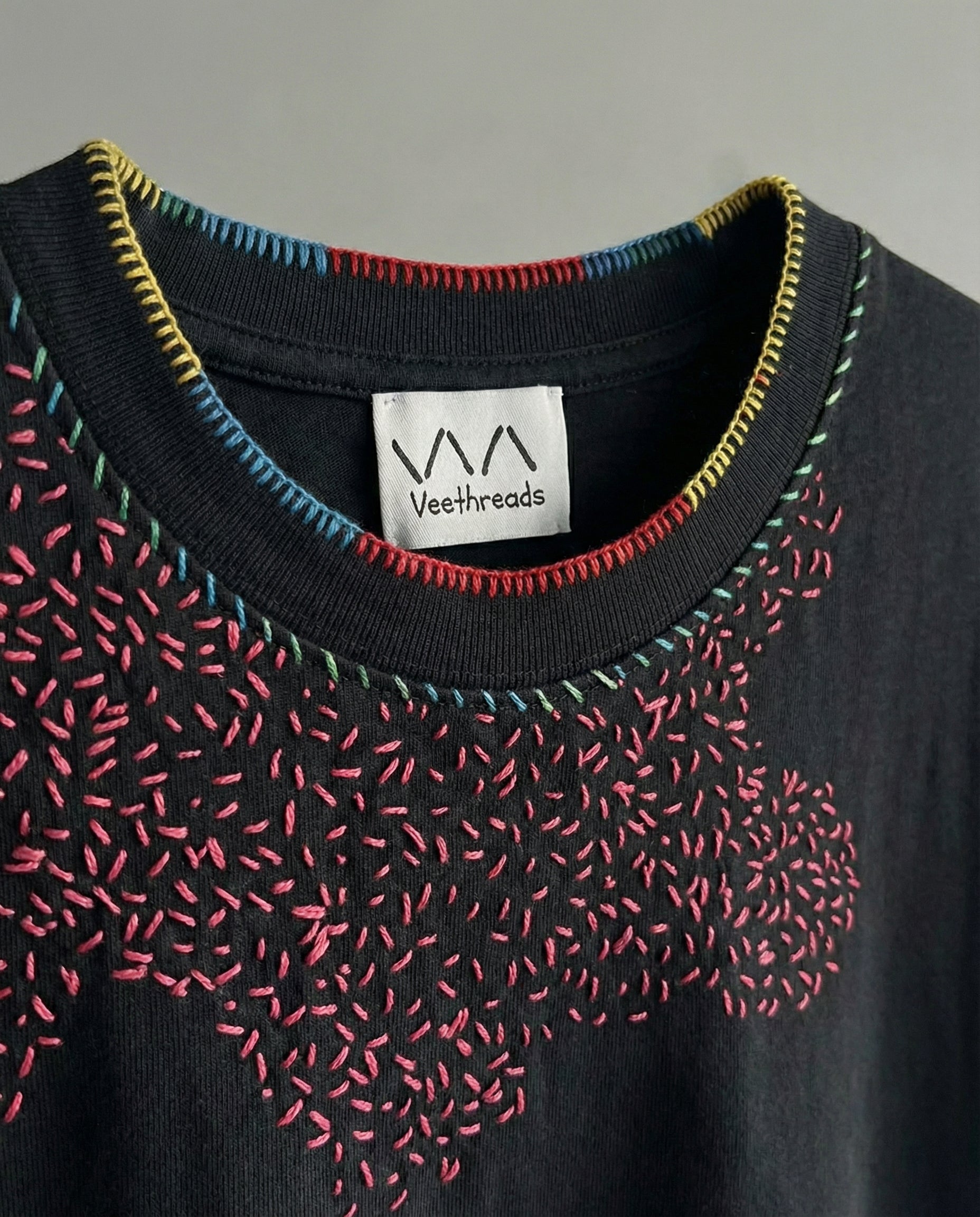 Black garment with colorful stitching and Veethreadz label on a gray background