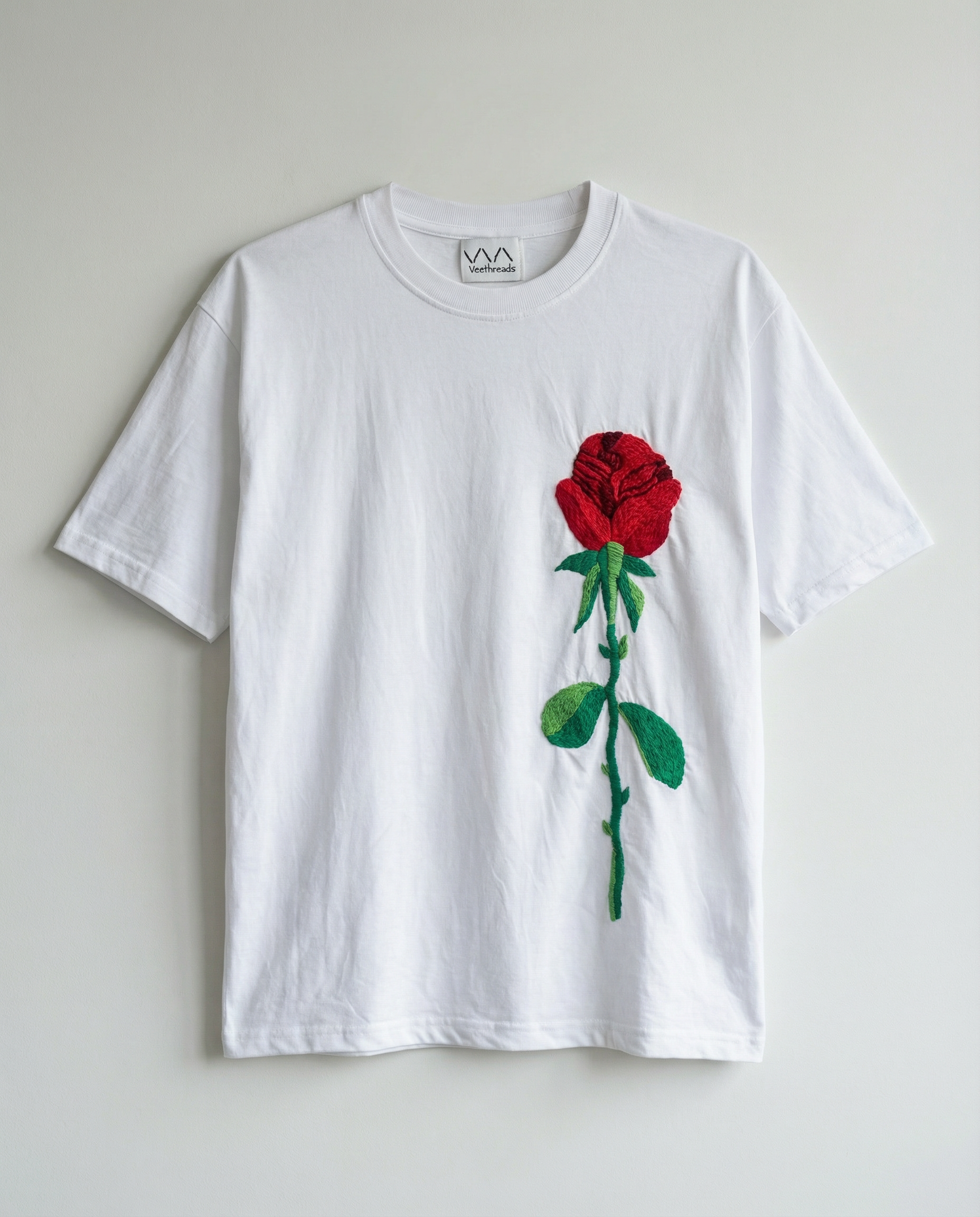 White t-shirt with a red rose hand embroidered on a light gray background
