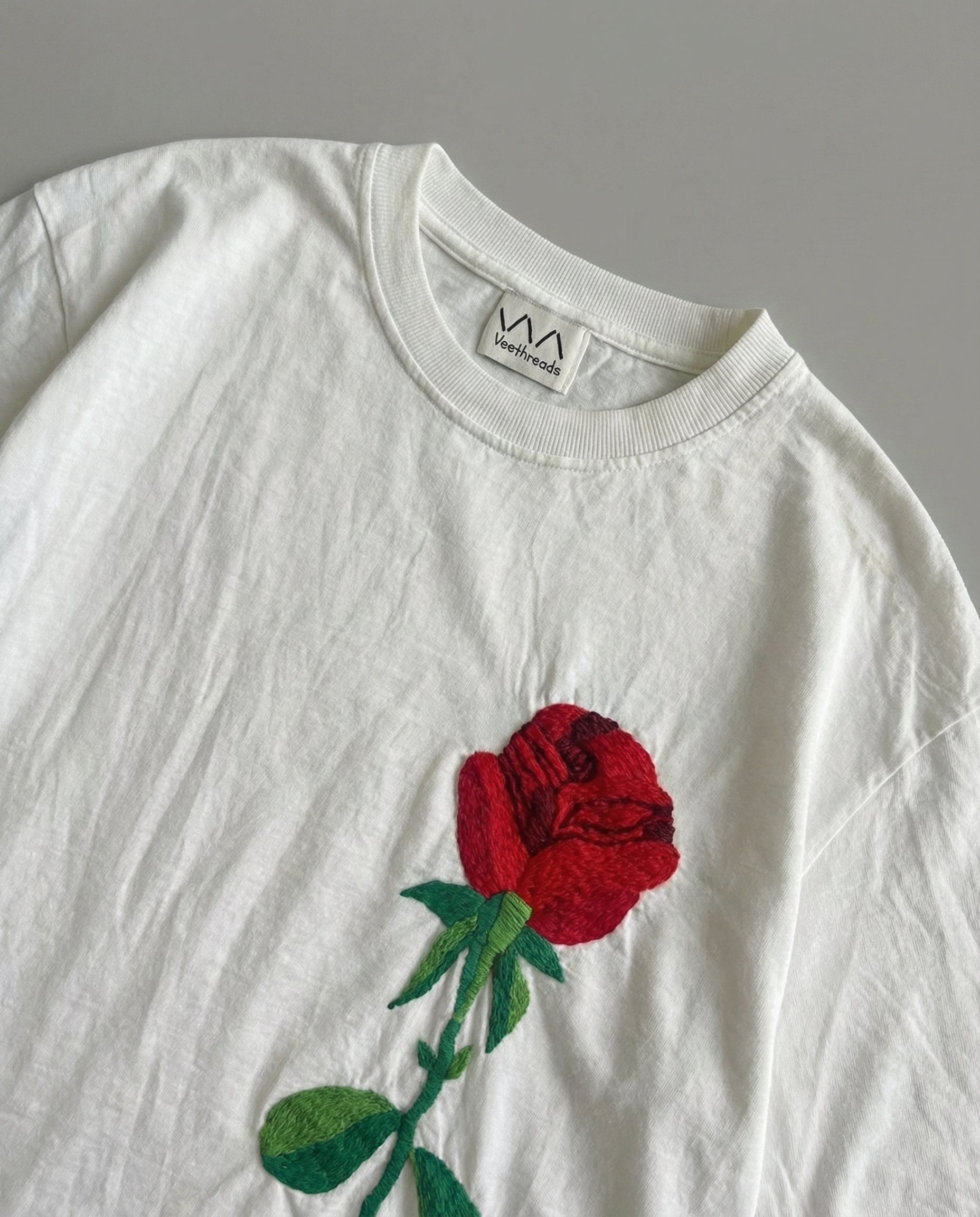 White t-shirt with a red rose embroidery on a gray background