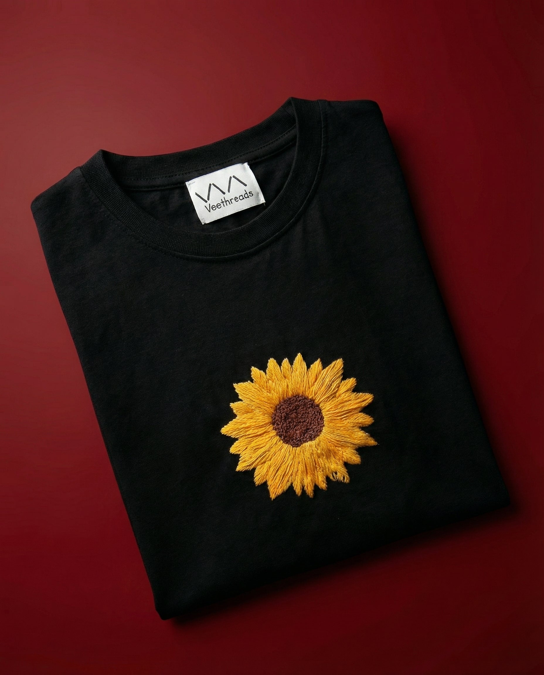 Black t-shirt with a yellow sunflower design embroidered on a red background