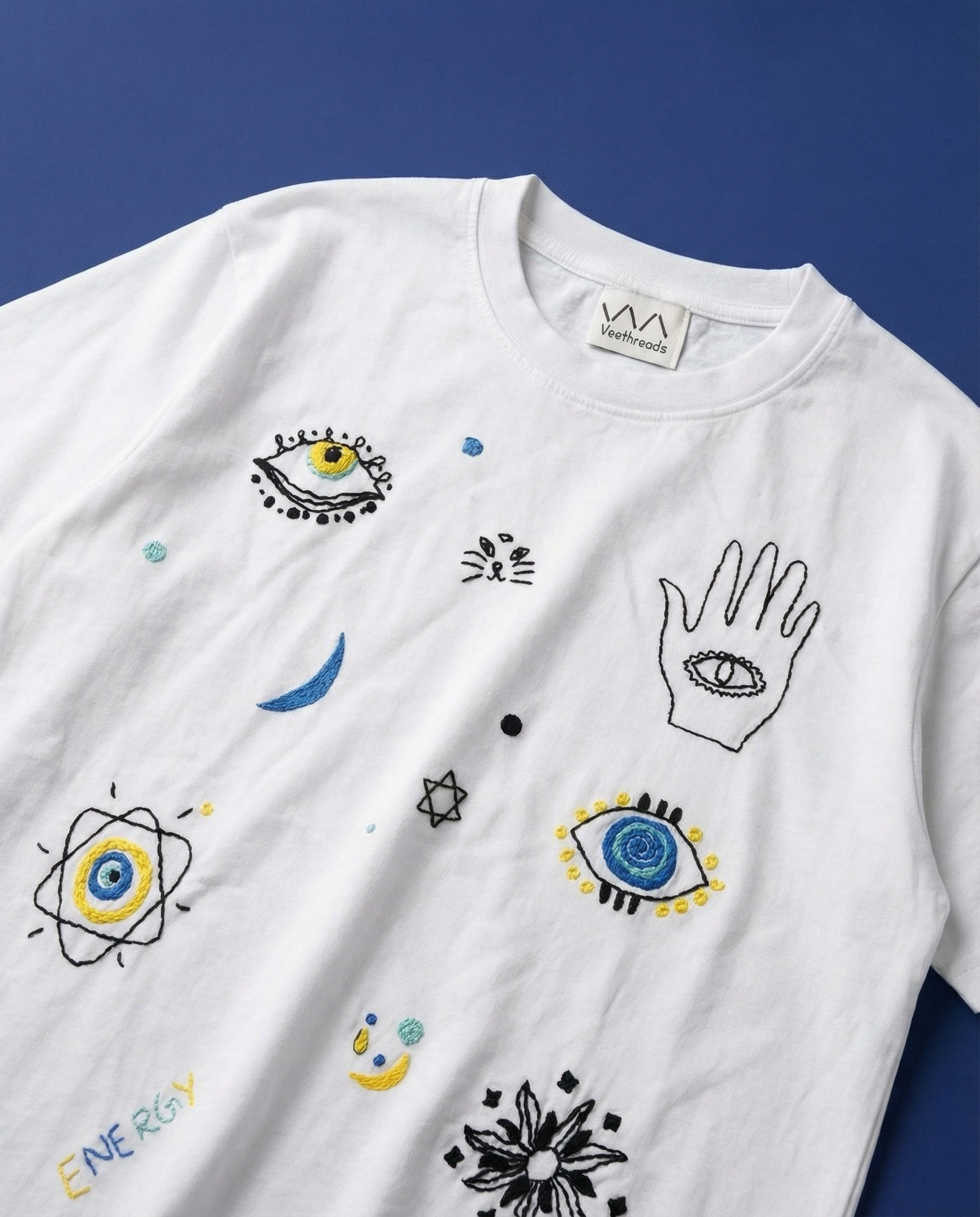 White t-shirt with various doodles embroidered and designs on a blue background