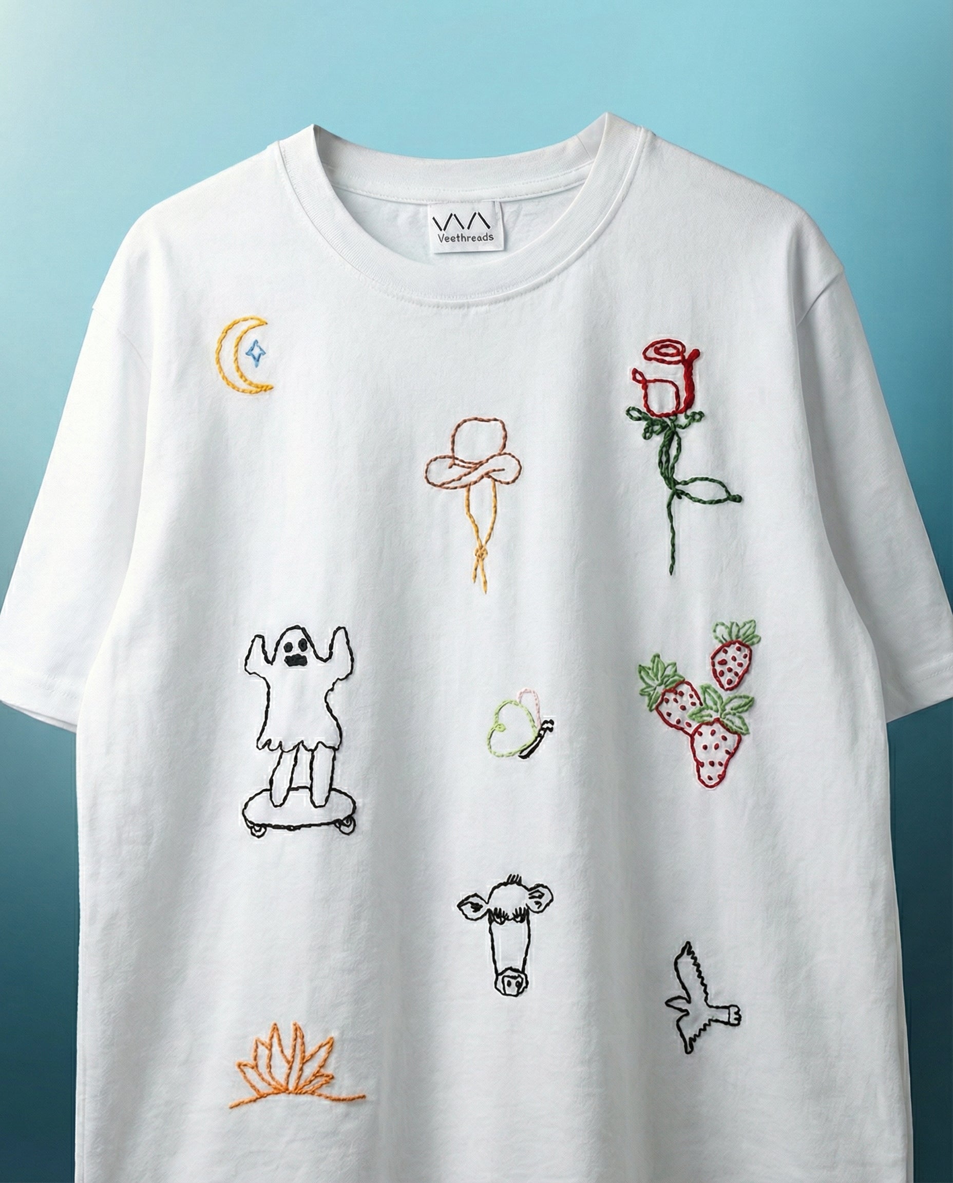 White t-shirt with embroidered designs on a blue background