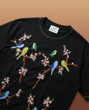 Black t-shirt with colorful bird and floral embroidery on a brown background