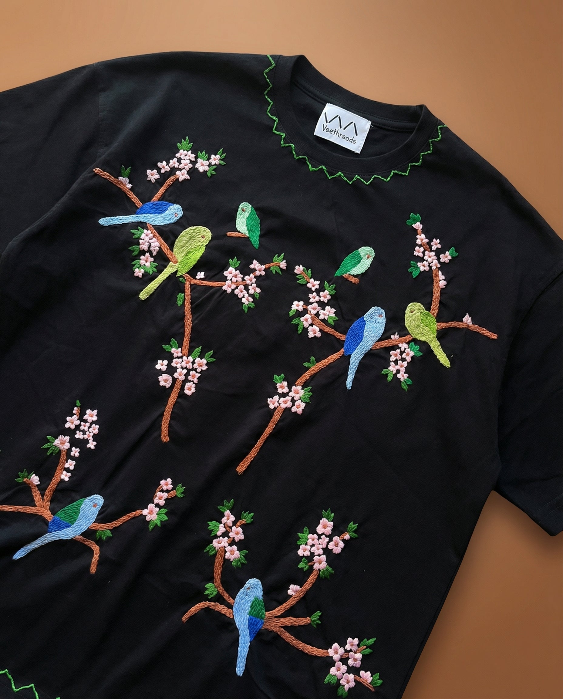 Black t-shirt with colorful bird and branch embroidery on a brown background