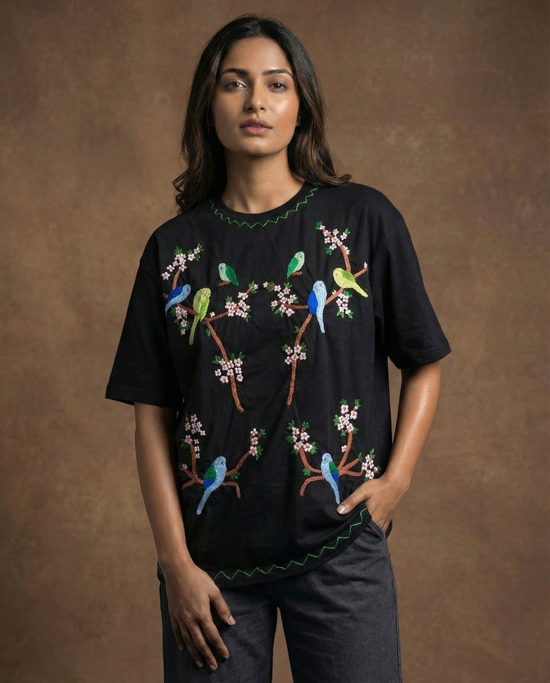 Woman wearing a black t-shirt with colorful bird and branch design against a brown background