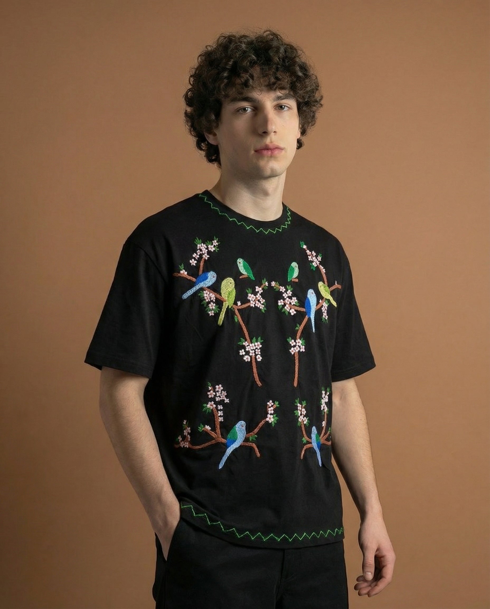 Person wearing a black t-shirt with colorful bird designs on a brown background