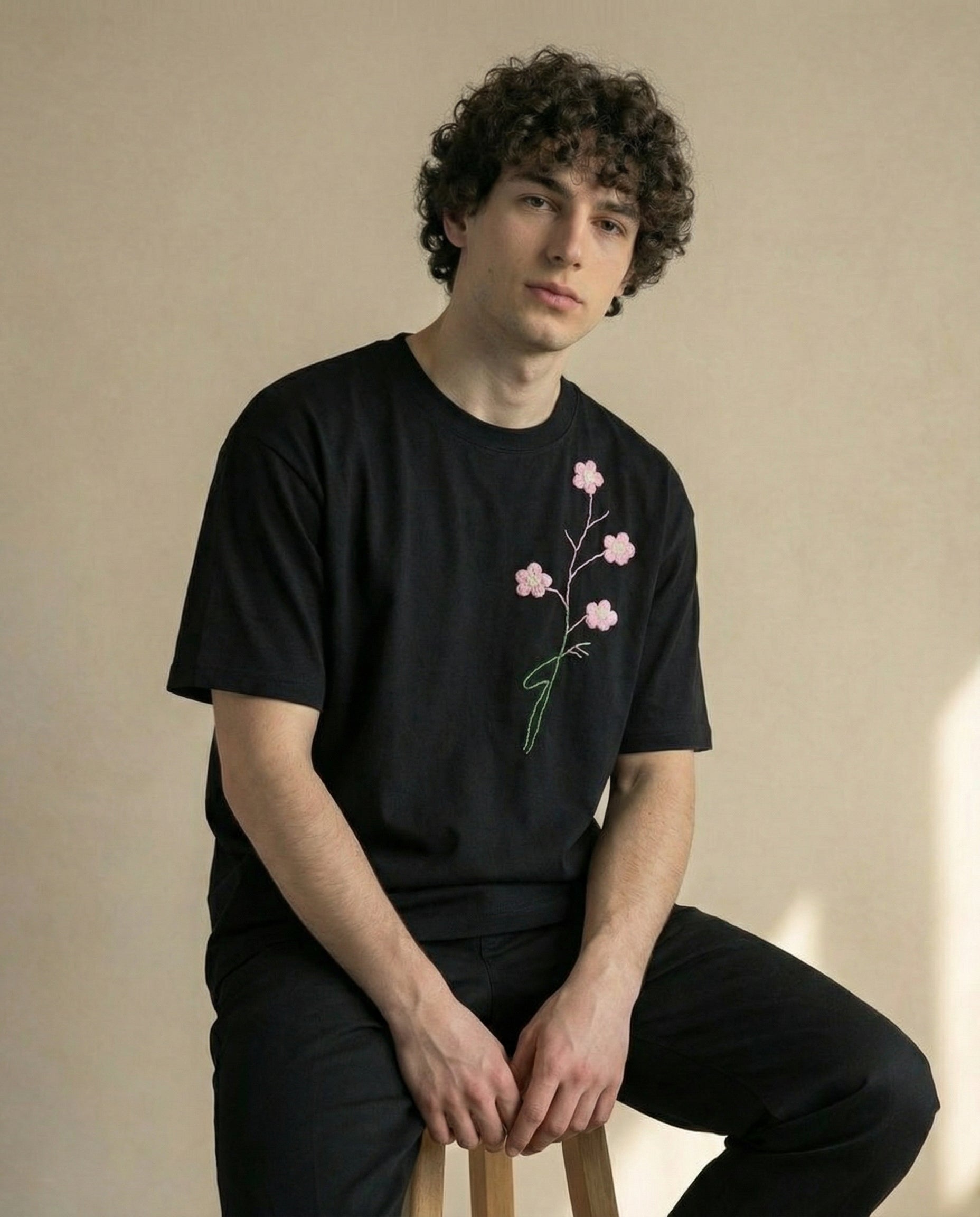Person wearing a black t-shirt with pink floral design against a beige background