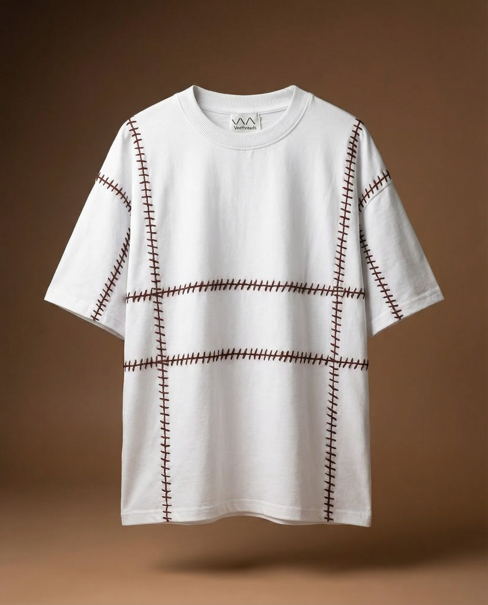 Geometric embroidered tee — white cotton tee with black geometric grid hand-embroidered pattern on brown background