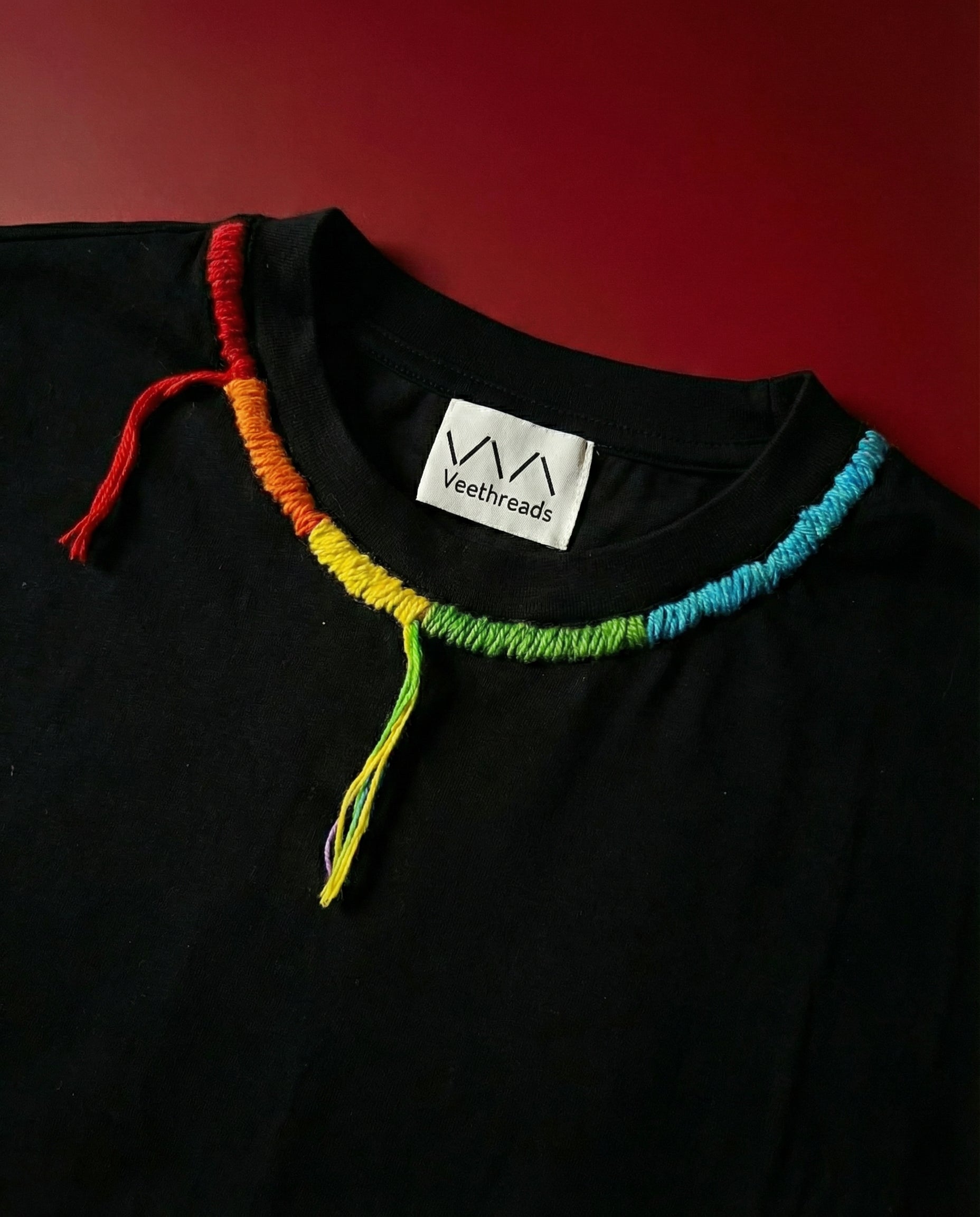 Black shirt with colorful yarn at neckline and Veethread brand label on a red background