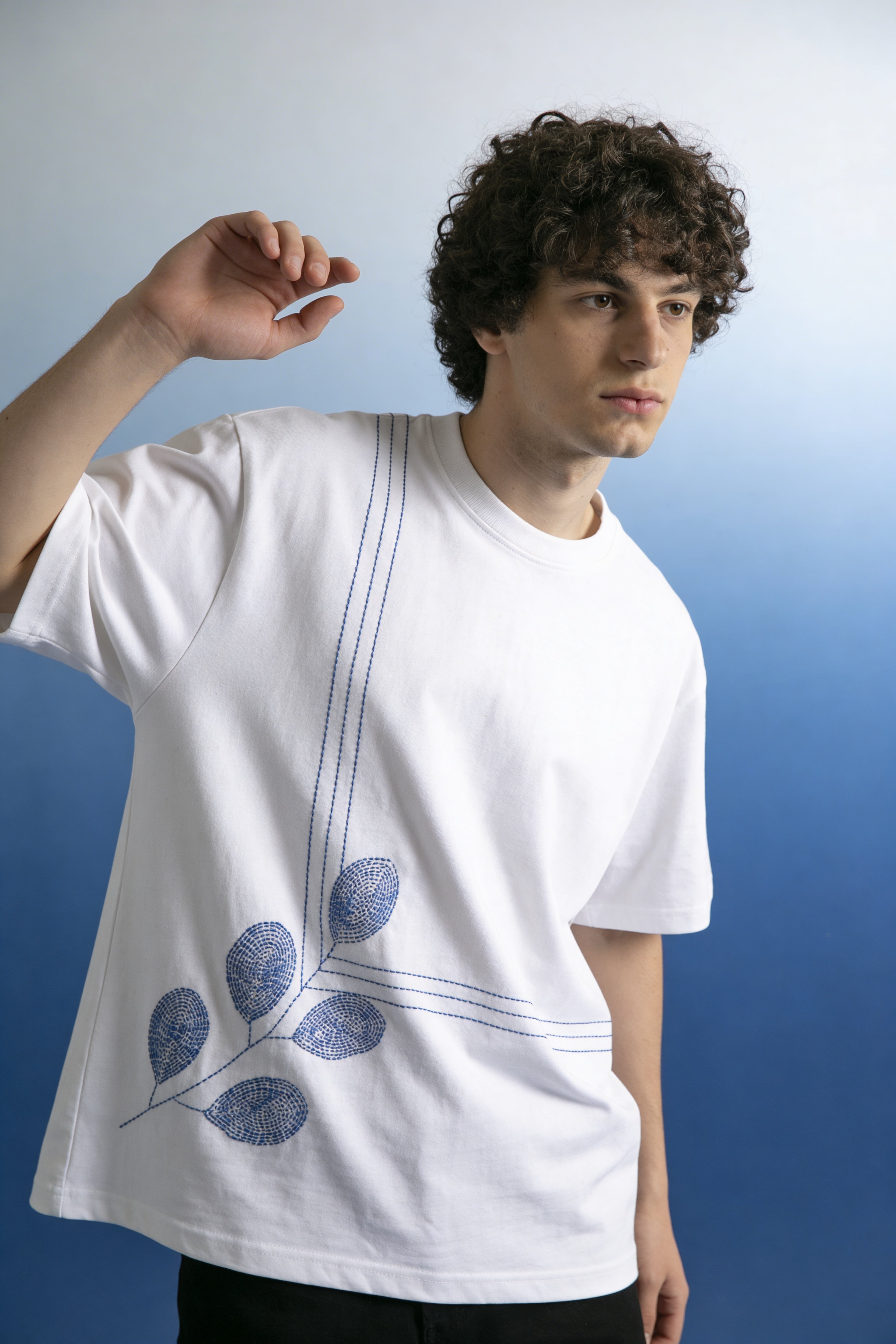 Person wearing a white t-shirt with blue leaf design against a gradient background