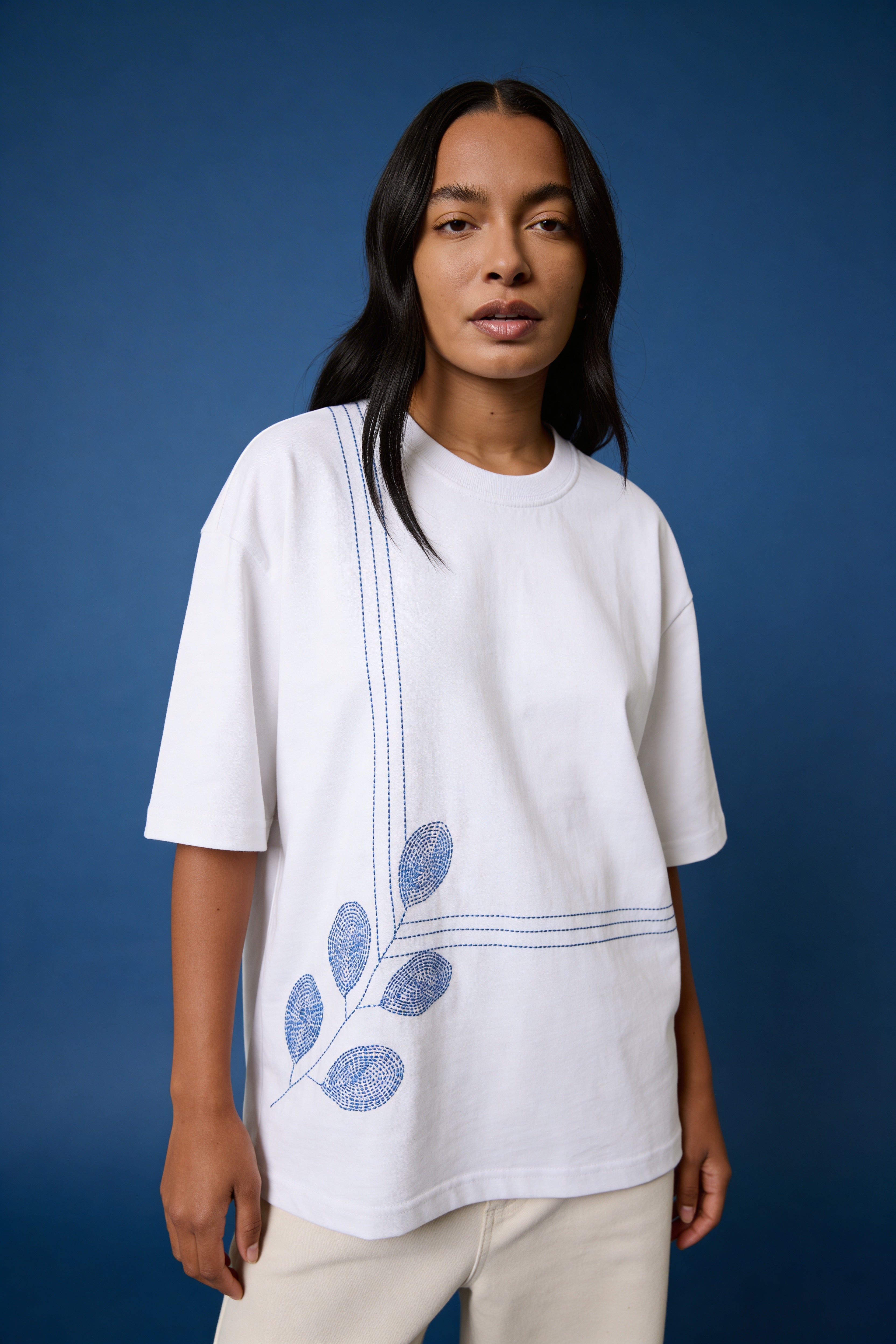 Woman wearing a white t-shirt with blue leaf design against a blue background