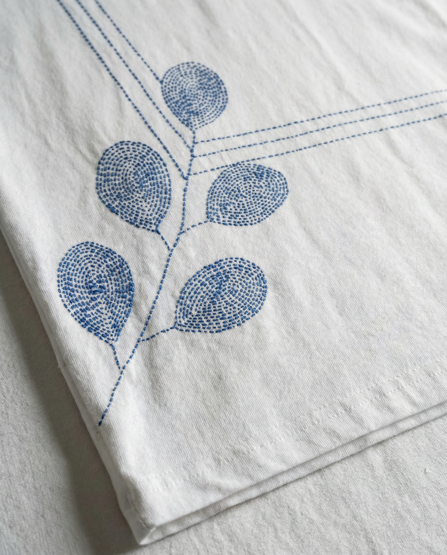 White fabric with blue embroidered leaf design on a white background