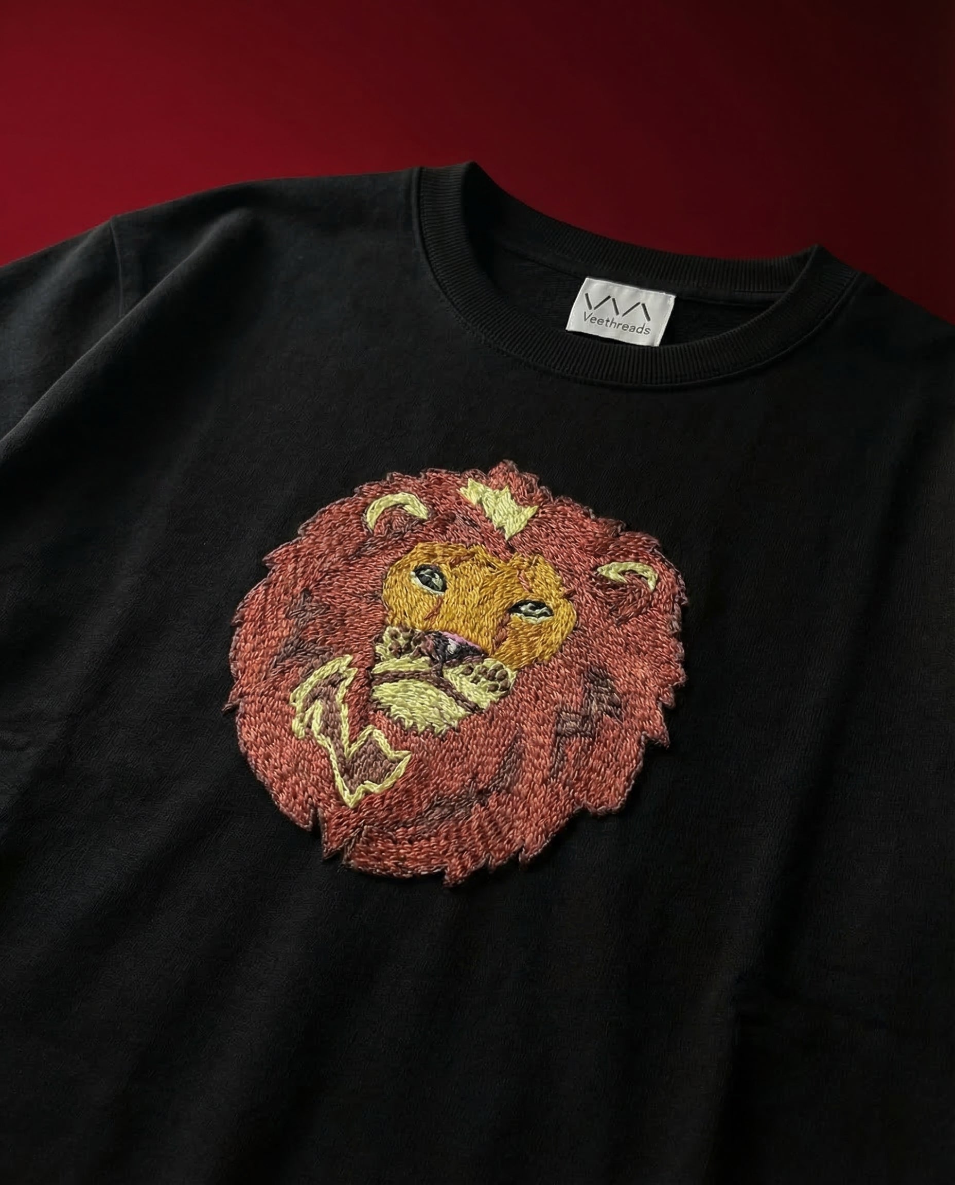 Black sweatshirt with a lion head design embroidered on a dark red background