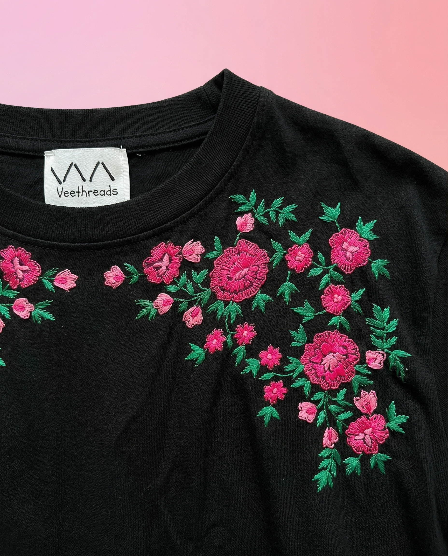 Black t-shirt with pink floral embroidery on a pink background