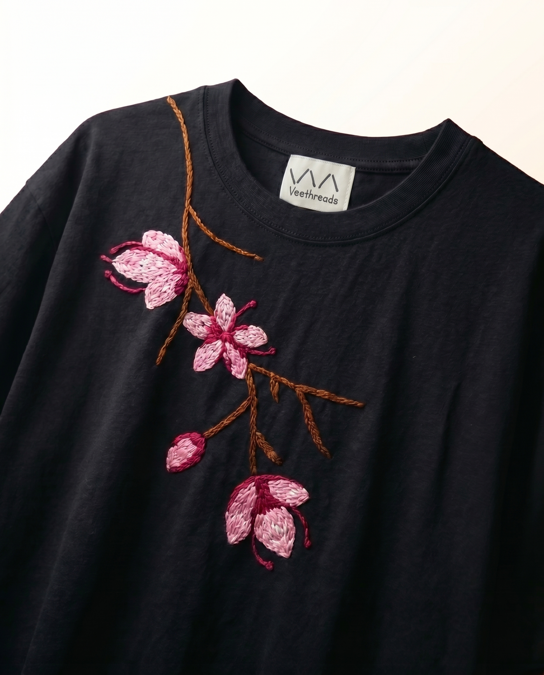 Hand-embroidered pink cherry blossom branch on navy blue cotton t-shirt — close-up of 3D satin stitch floral embroidery by Vee Threads women artisans