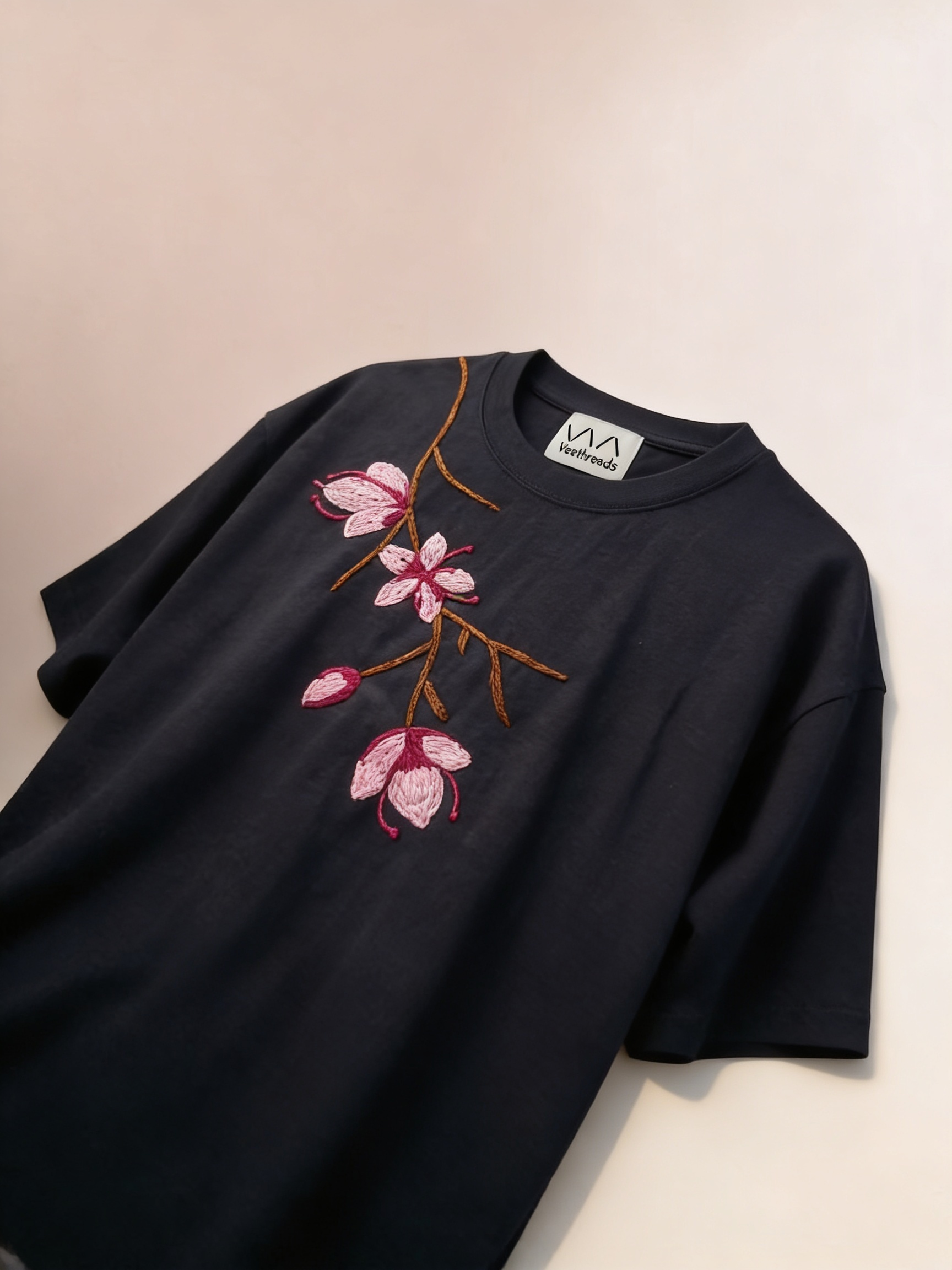 Cherry blossom embroidered sweatshirt — black sweatshirt with pink cherry blossom floral embroidery on beige background