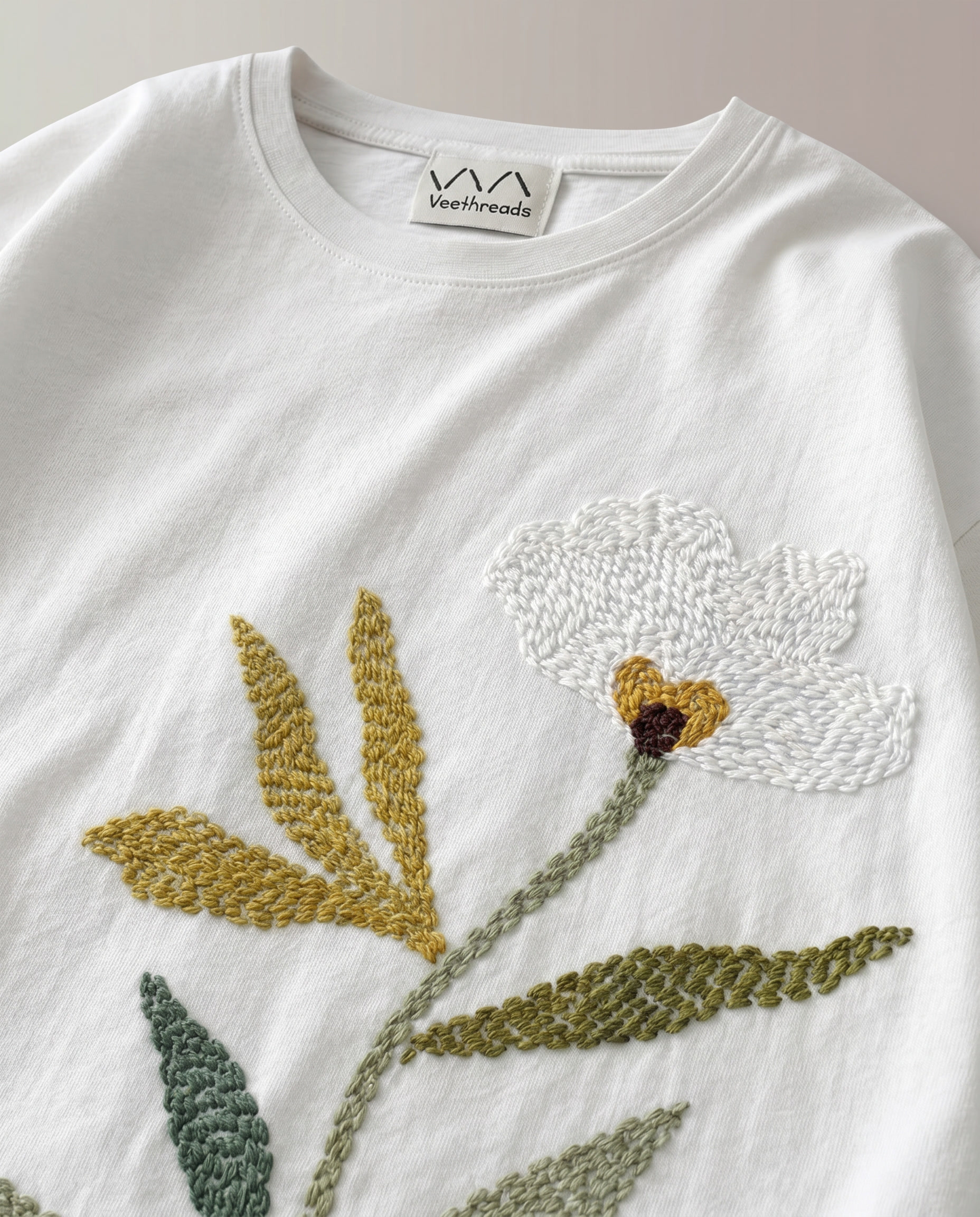 Close-up of hand embroidered green leaves in teal, sage and olive thread on The Botanist Tee by Veethreads — artisan embroidery made in India