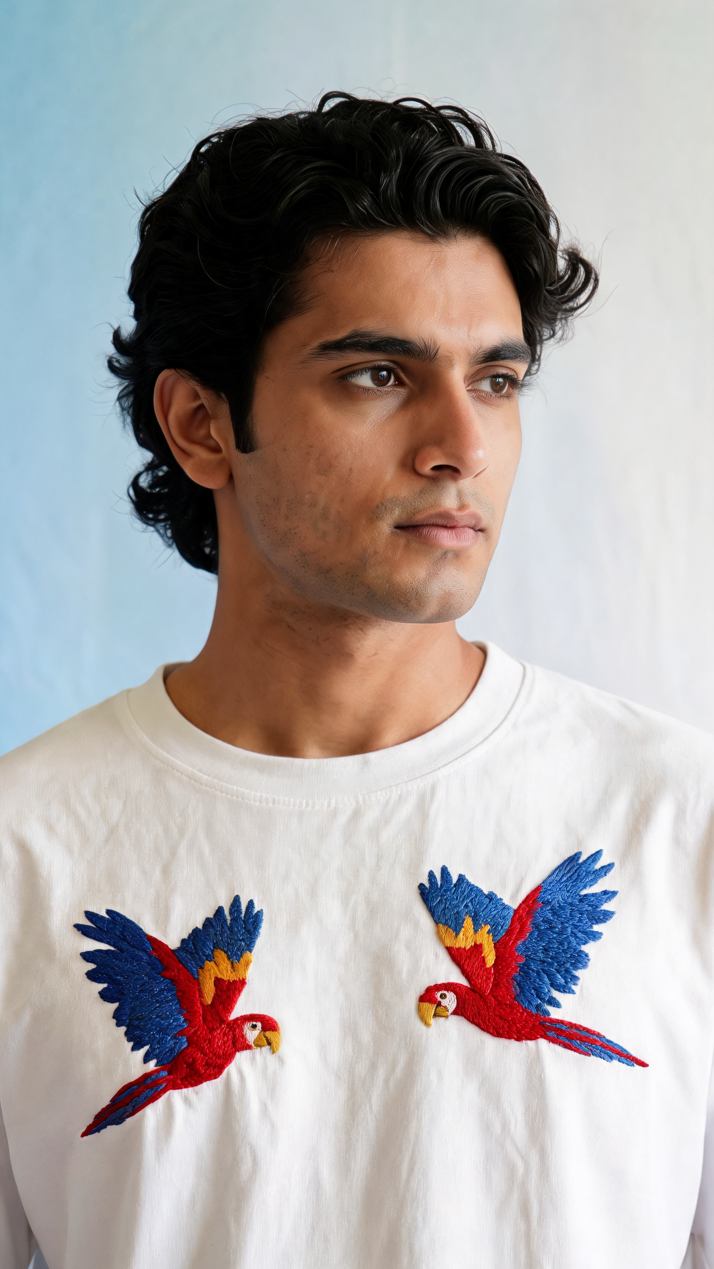 Man wearing a white t-shirt with embroidered parrot designs against a light blue background