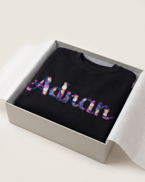Black sweatshirt with colorful 'Adrian' custom name text in a box on a white background