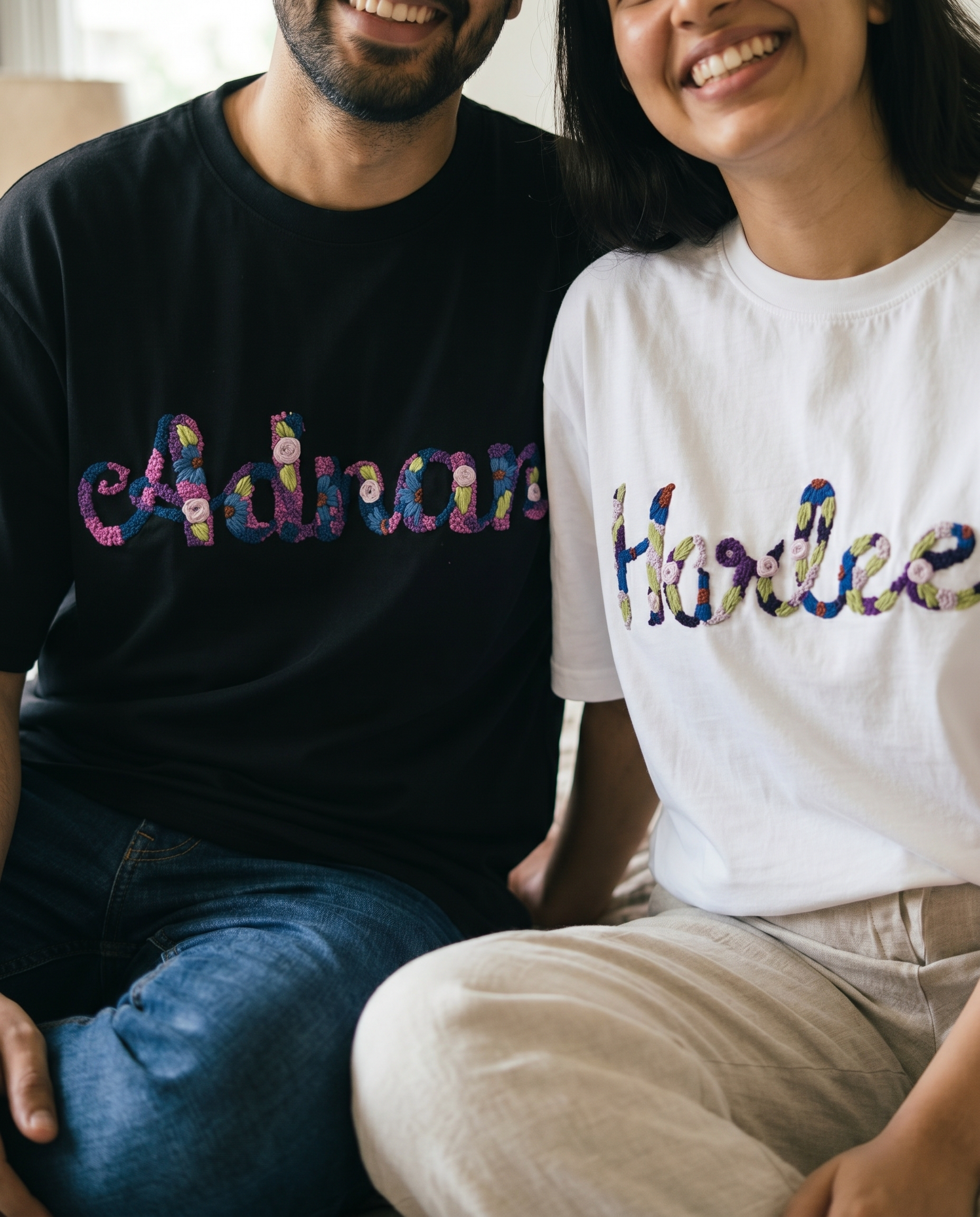 Two people wearing t-shirts with custom colorful text, sitting close together.