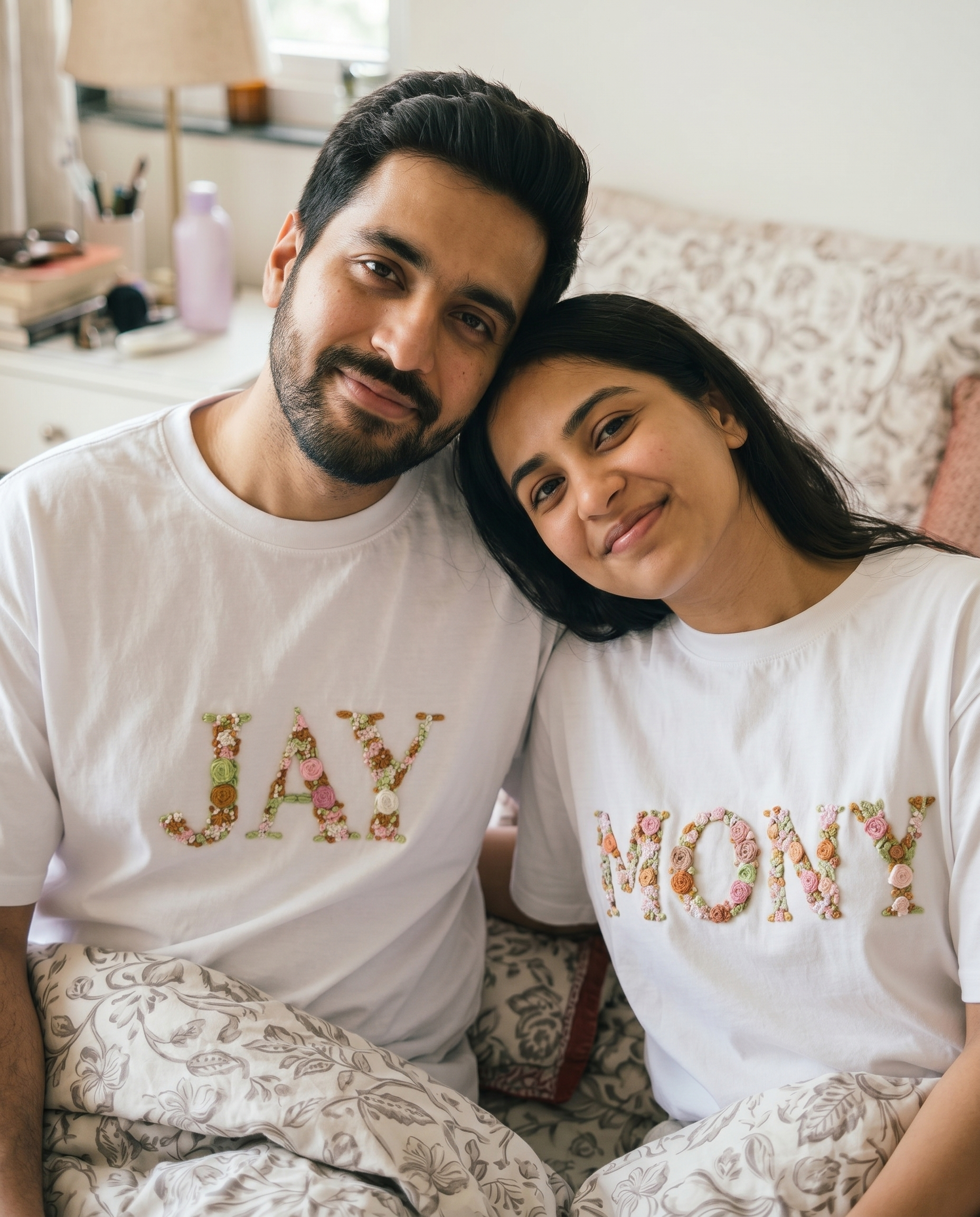 Man and woman sitting on a couch wearing matching t-shirts with floral text.