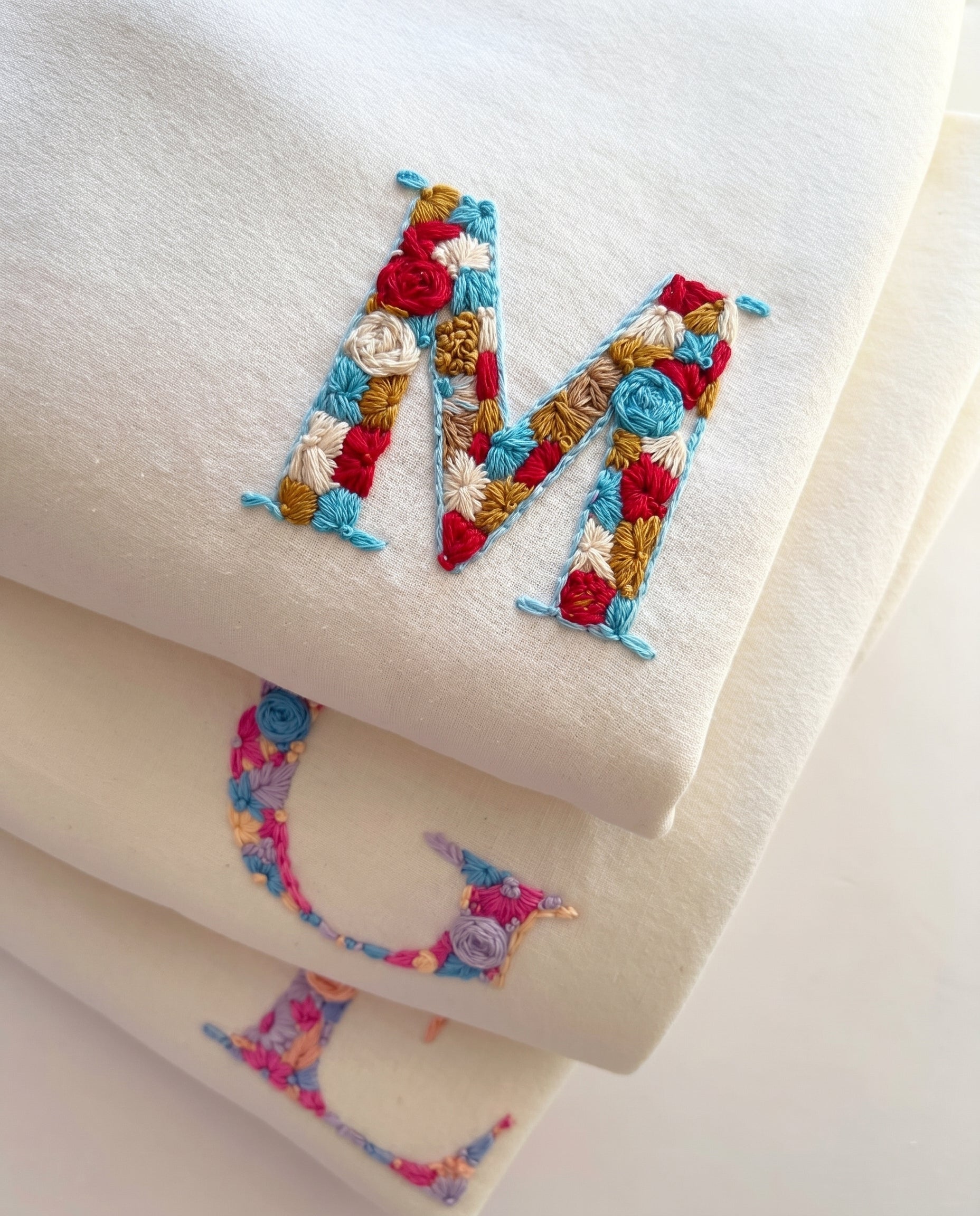 Colorful embroidered letter 'M' on a white fabric background