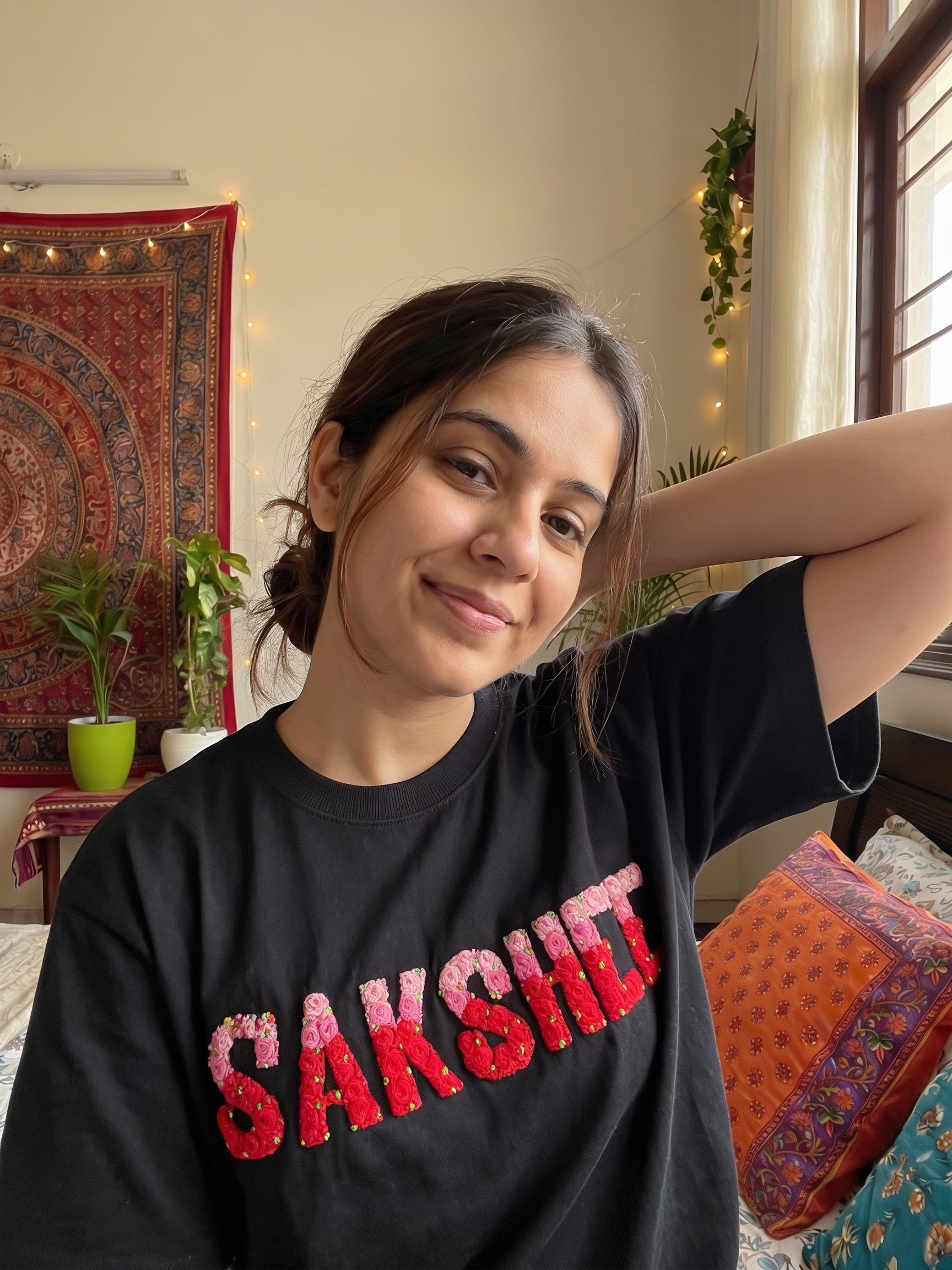 Person wearing a black t-shirt with 'SAKSHIET' in red, sitting in a room with decorative elements.