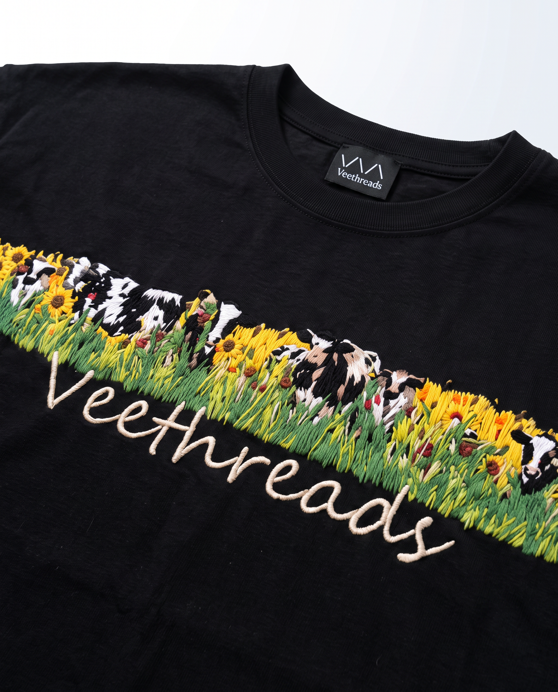 Detail of hand stitched cows, sunflowers and grass on black cotton with Veethreads cursive script