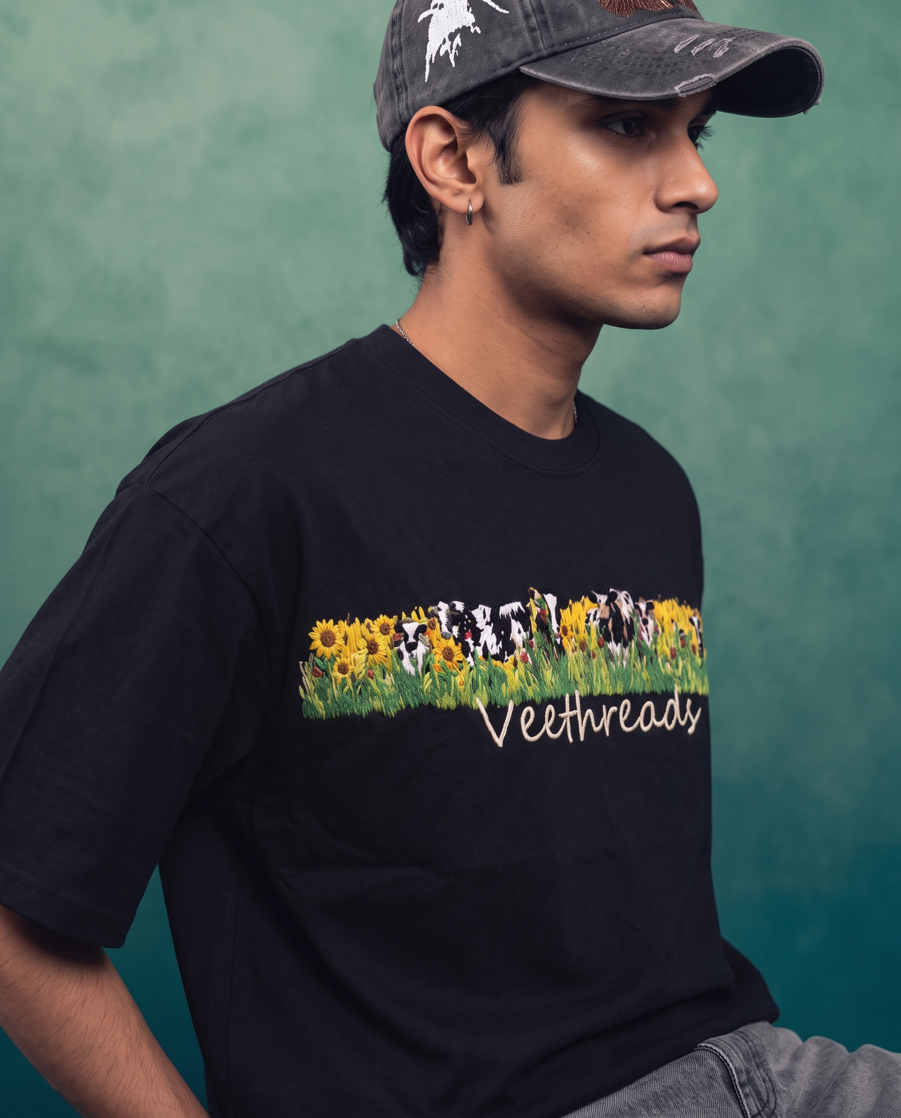 Close view of model in black embroidered oversized cotton t-shirt with grey cap