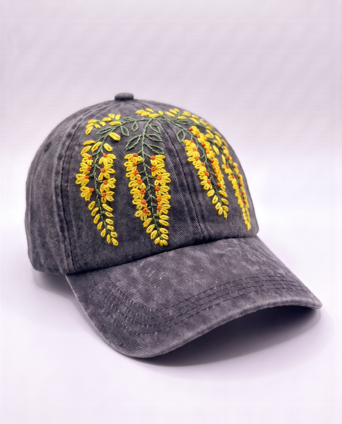 Angled view of the hand-embroidered amaltas cap showing the blossom sprays falling across the front panels