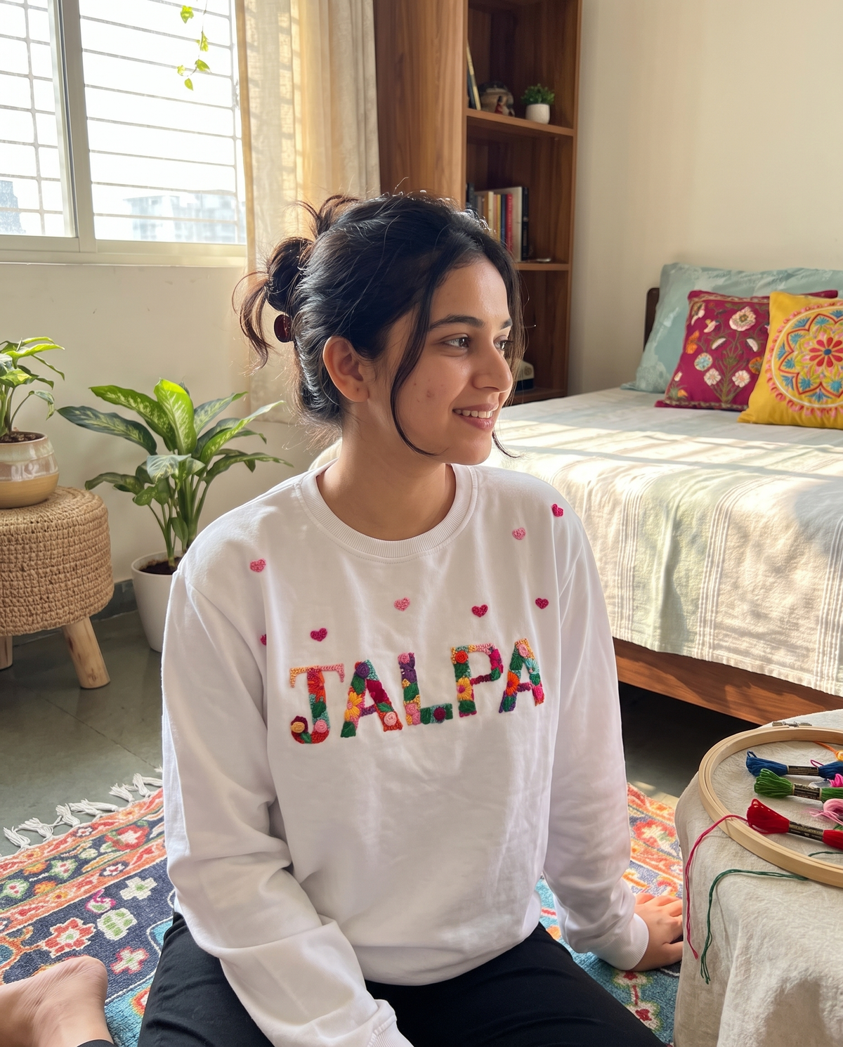 Young woman wearing a custom name and hearts embroidered sweatshirt in her room, relaxed loose fit