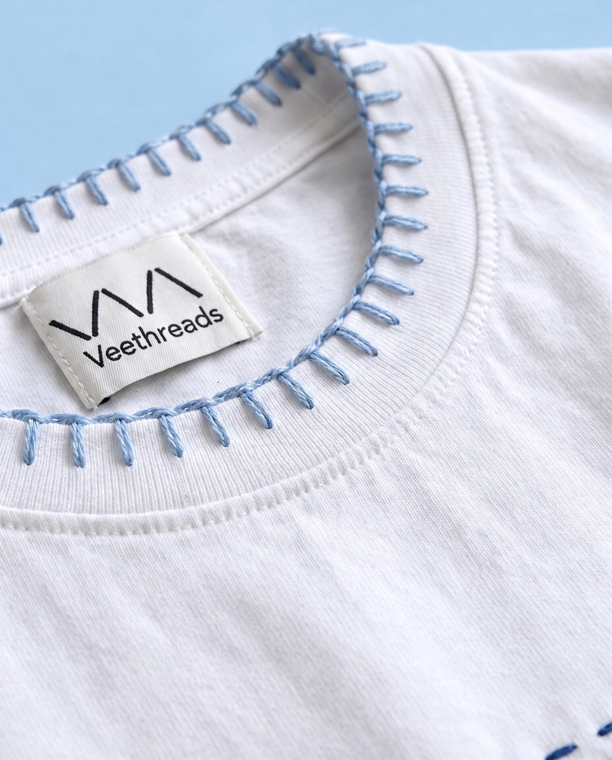 Close-up of light blue blanket stitch hand-embroidered around the collar of a white cotton t-shirt