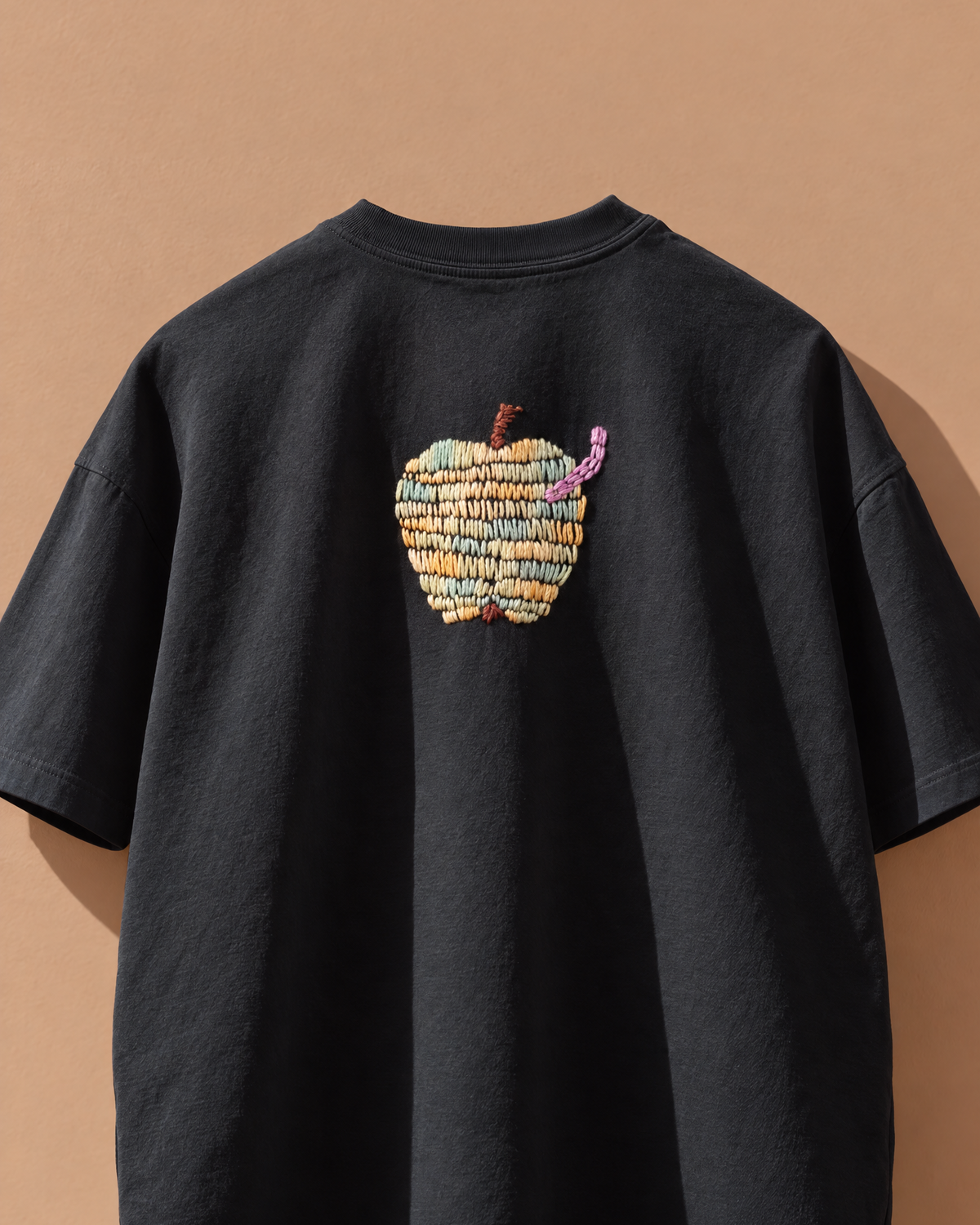 Front of a black 220 GSM cotton oversized tee with a hand-stitched apple just below the collar