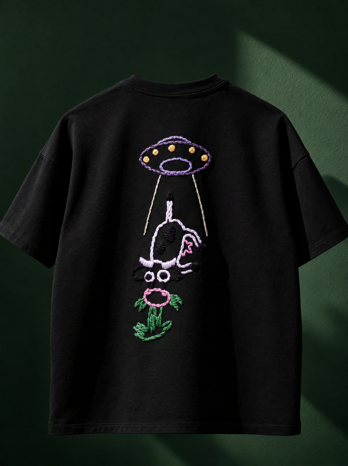 Black 220 GSM cotton oversized tee with a hand-stitched UFO abducting a cow, full view on a green background