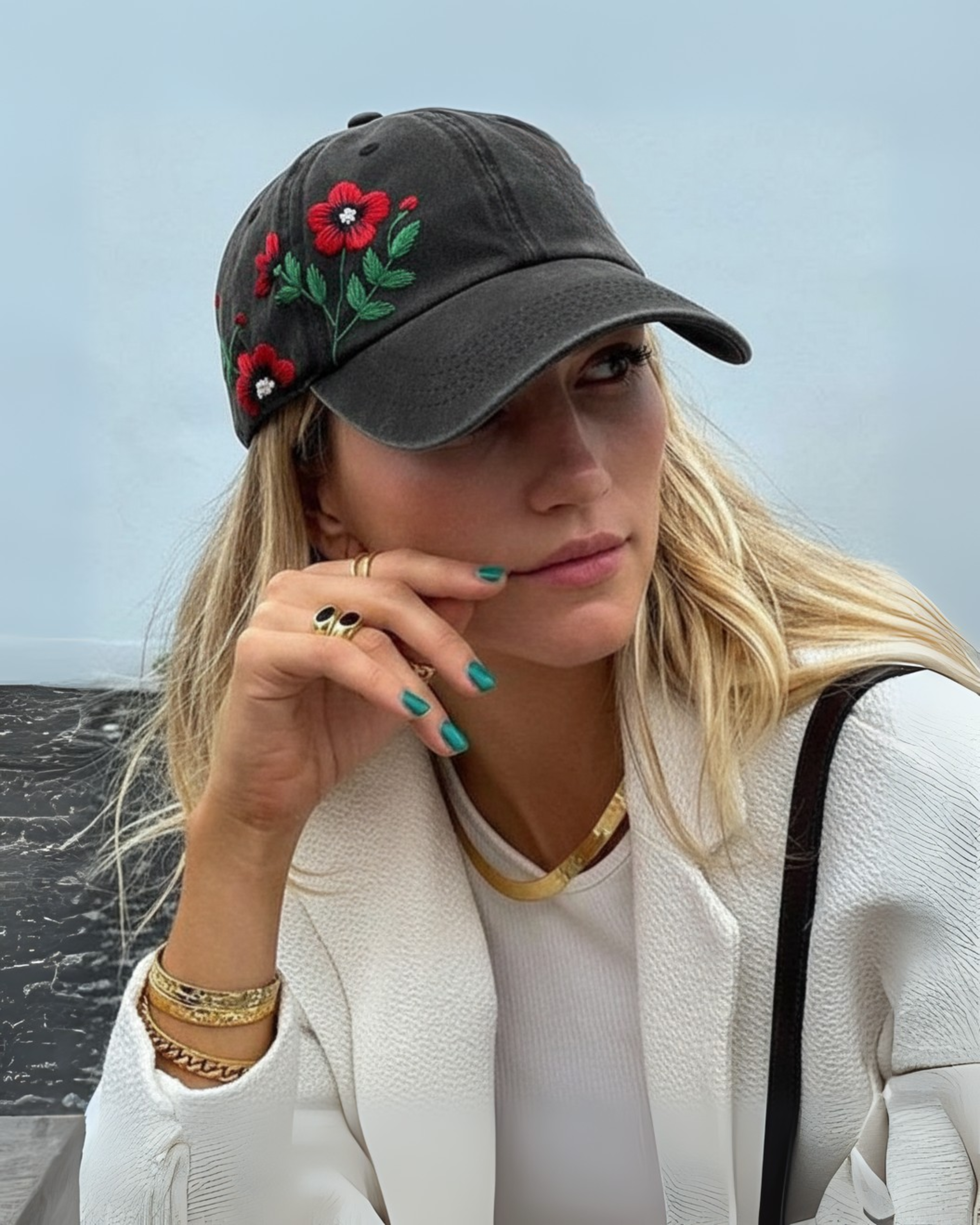 Woman wearing a dark gray cap with floral embroidery, standing against a blurred natural background.