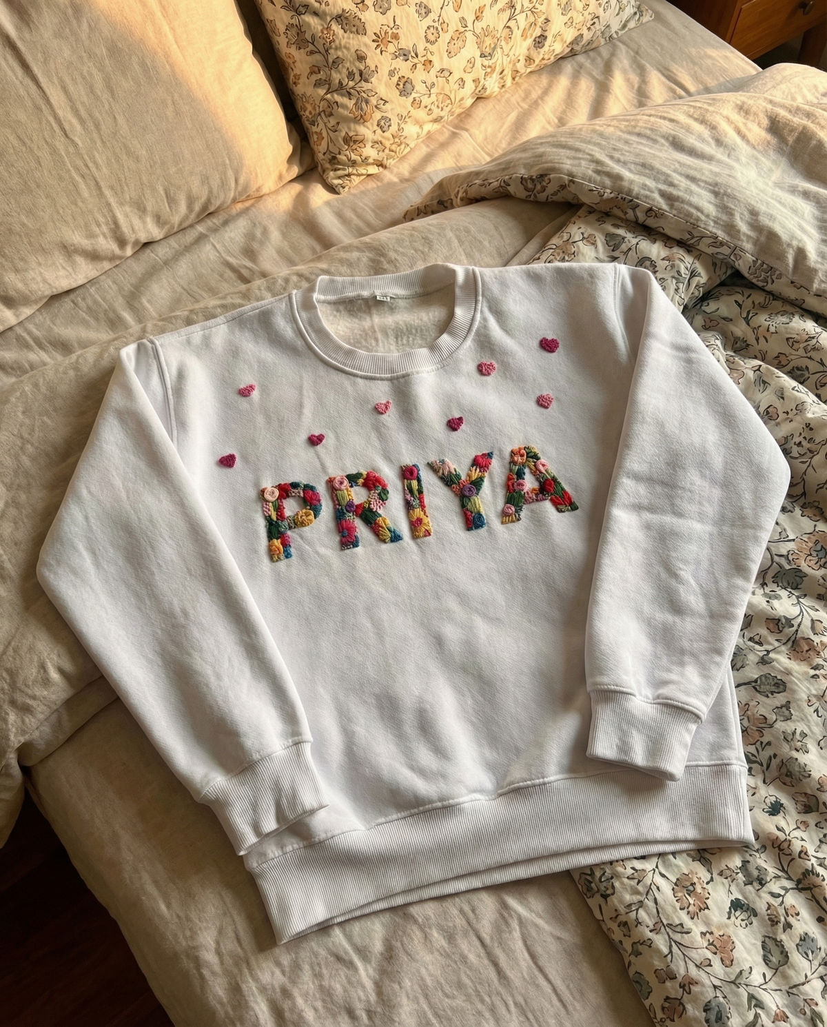 Name hand-stitched in colourful script lettering across a white cotton sweatshirt