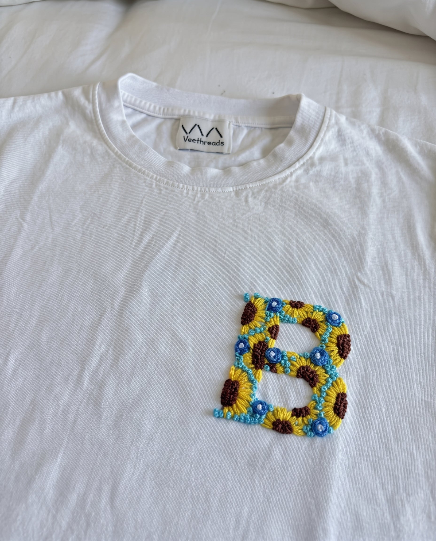 Hand-embroidered floral initial, sunflowers and blue flowers, on a white cotton tee by Vee Threads