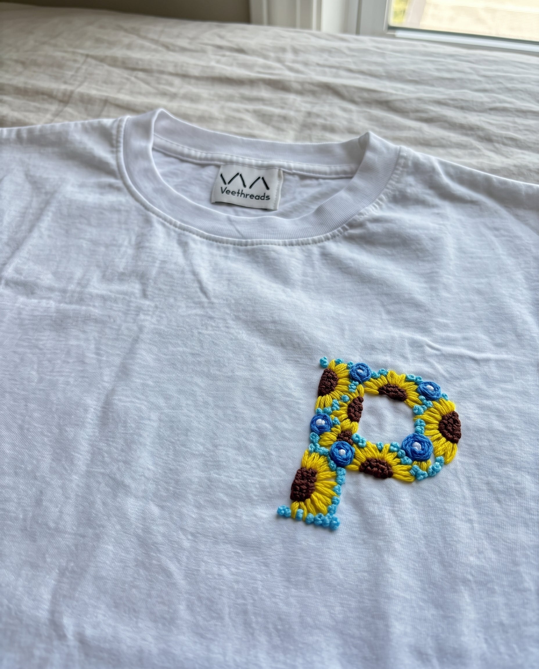 Hand-embroidered floral initial, sunflowers and blue flowers, on a white cotton tee by Vee Threads